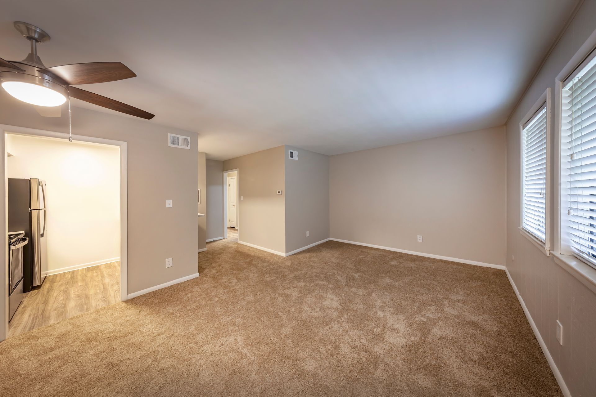 An empty living room with a ceiling fan and a refrigerator.