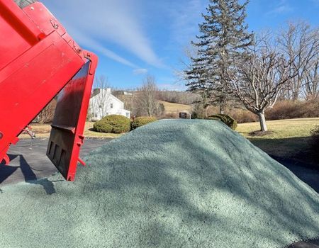 Red dump truck unloading a pile of green gravel on a paved driveway.