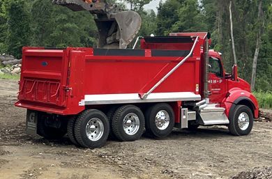 Red dump truck being loaded with material by an excavator in an outdoor setting.