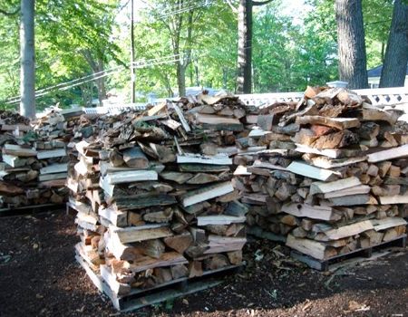 Piles of split firewood stacked on wooden pallets outdoors, ready for use.