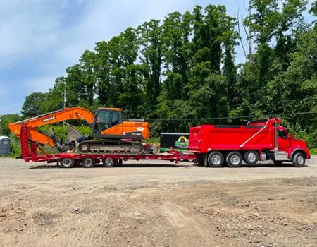 A red dump truck is carrying an excavator on a trailer.