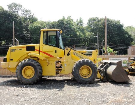 Yellow New Holland LW170.B wheel loader parked outdoors. It has a large bucket, large tires, and a cab.