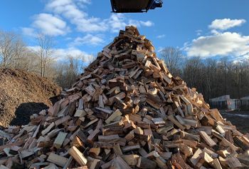 Large pile of firewood against a blue sky, possibly being unloaded from above.