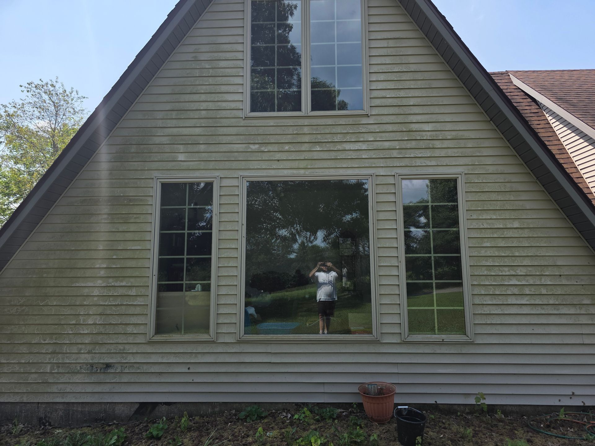 Front view of a beige A-frame house with large windows and a small potted plant by the porch.