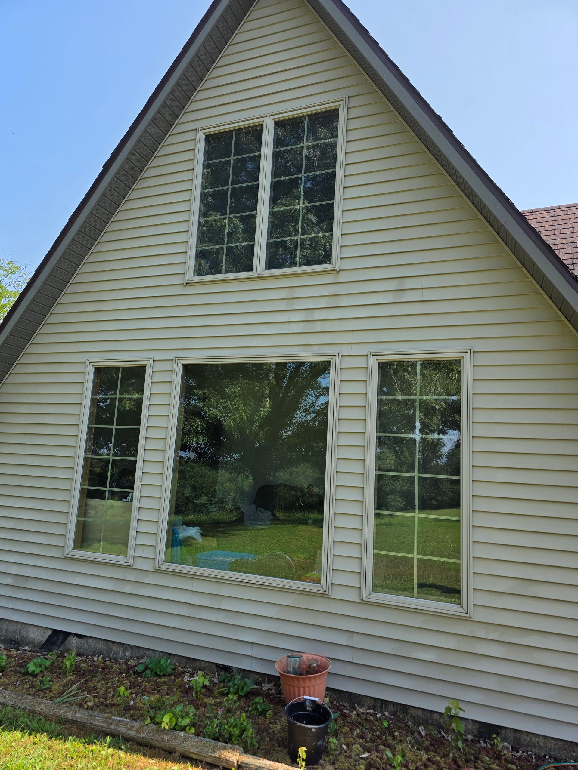 Cream-sided house with gabled roof and tall windows, viewed from the side in daylight.