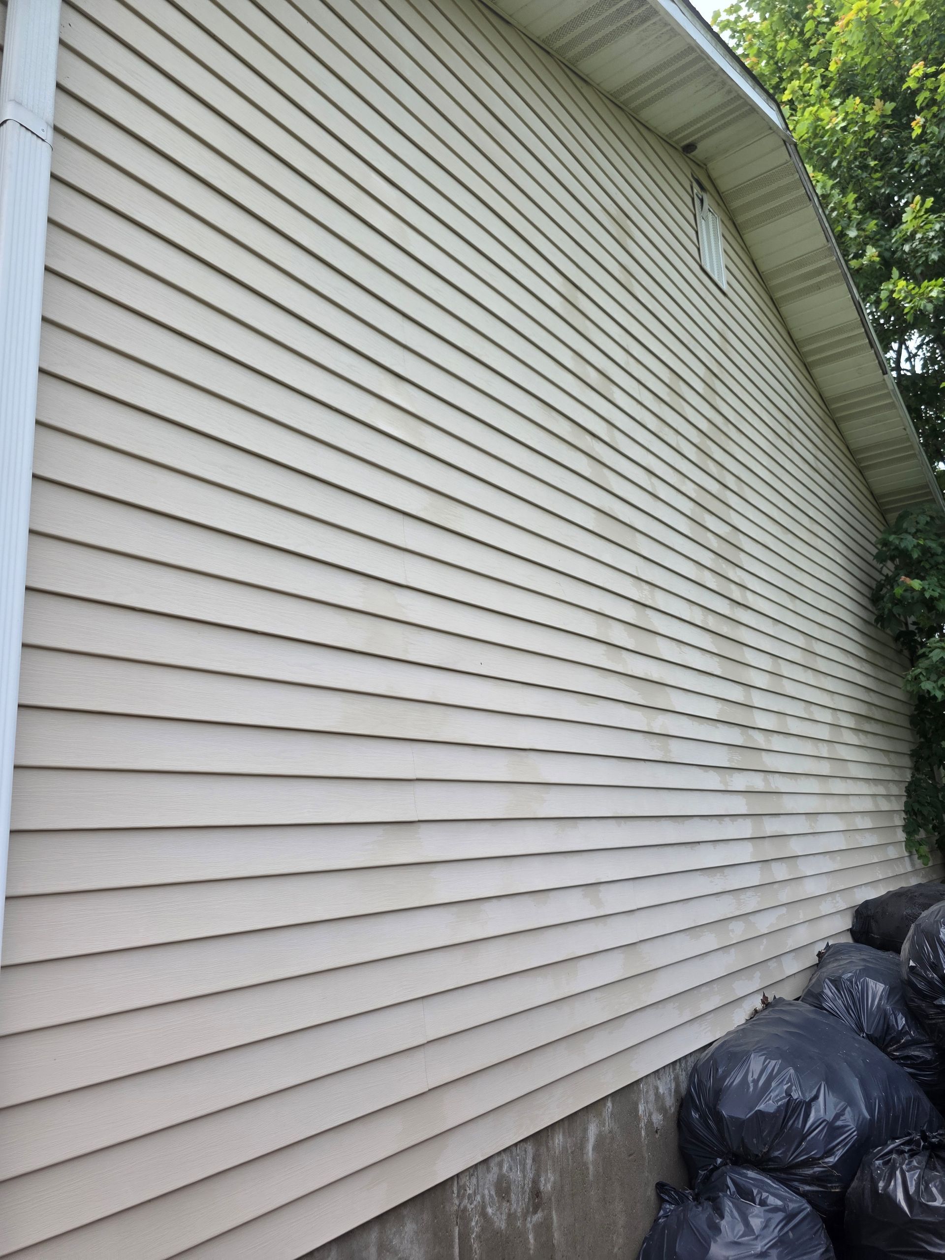 White vinyl-sided exterior wall with trash bags stacked along the bottom edge outside.