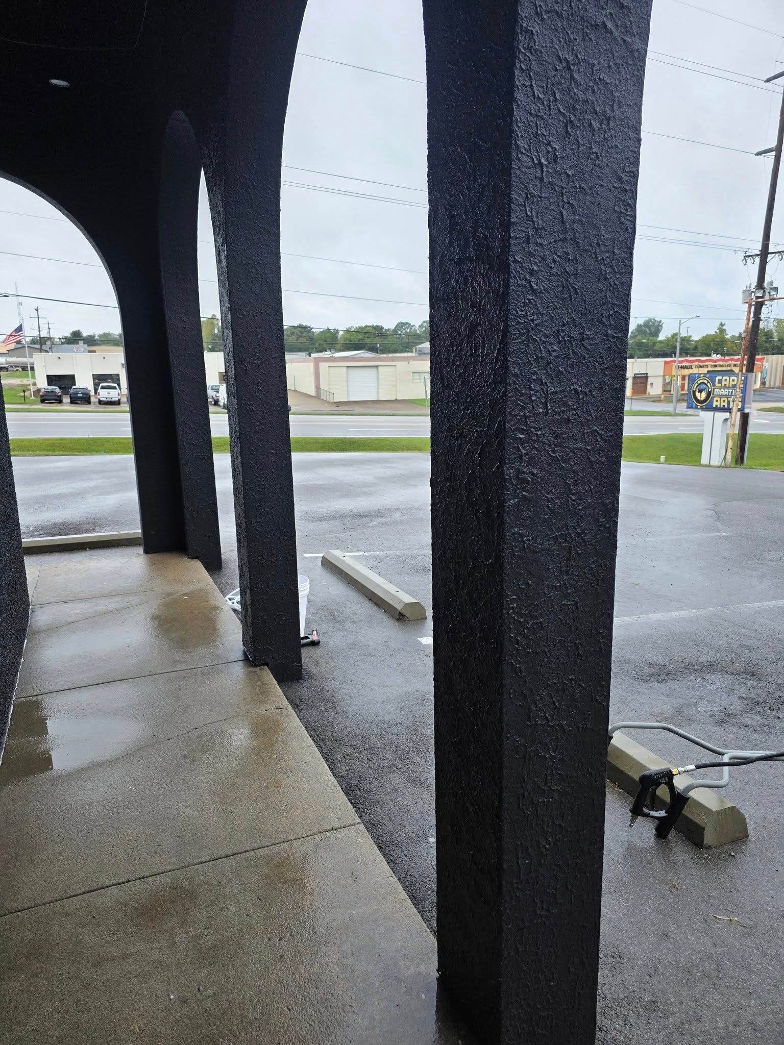 Rainy sidewalk under a covered storefront, with dark columns, wet pavement, and a cloudy street outside.