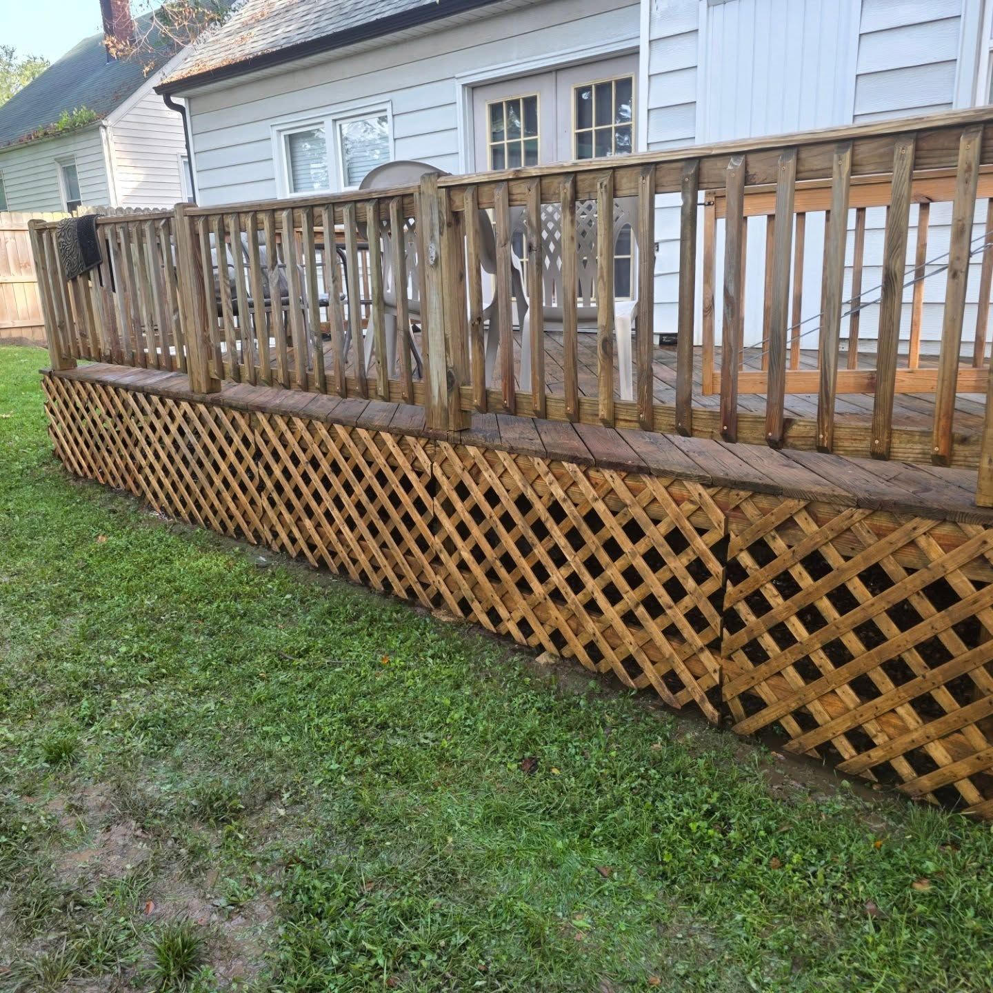 Wooden deck with railing and lattice skirting beside a white house and green lawn.