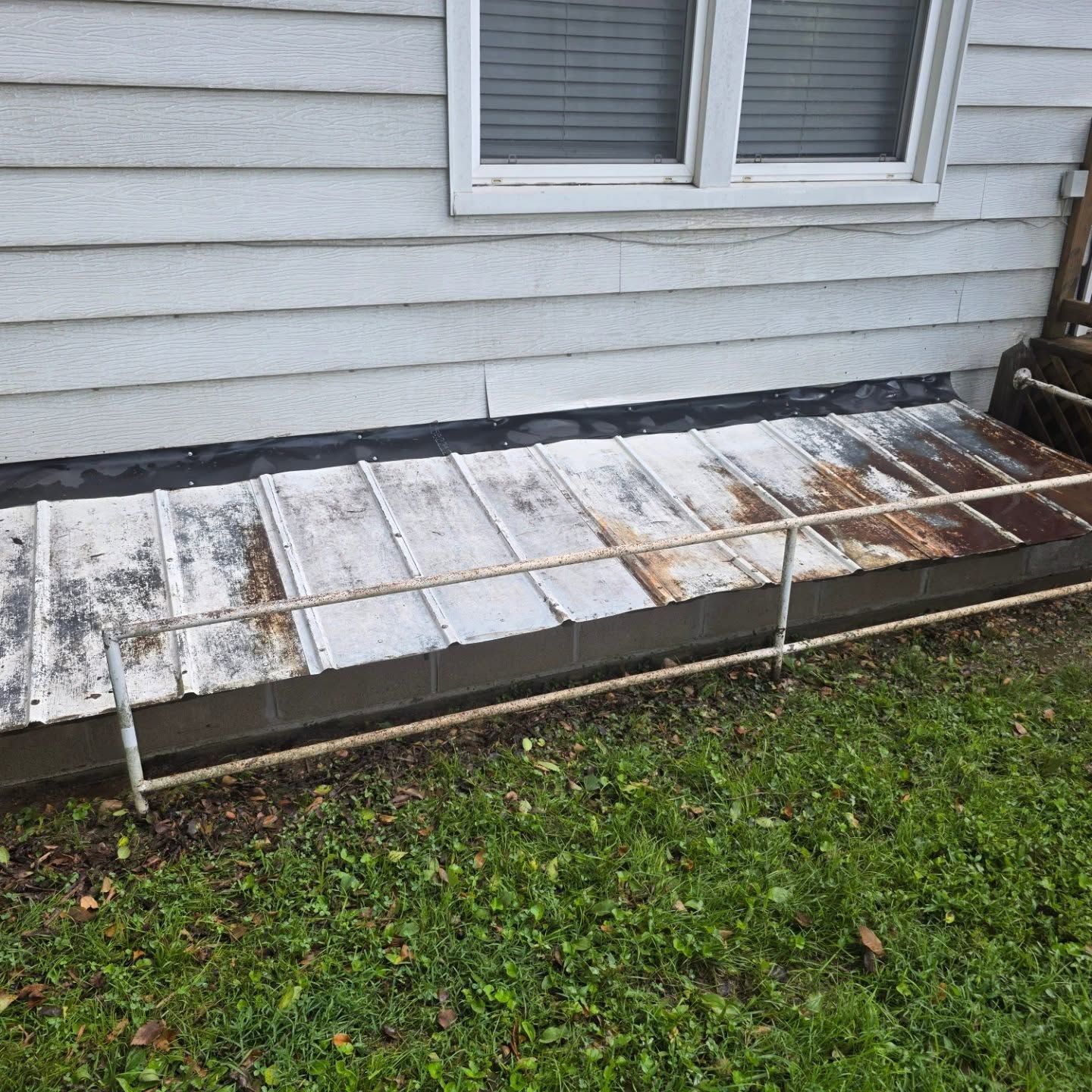 Snow-dusted wooden walkway beside a gray house with a window and grass below
