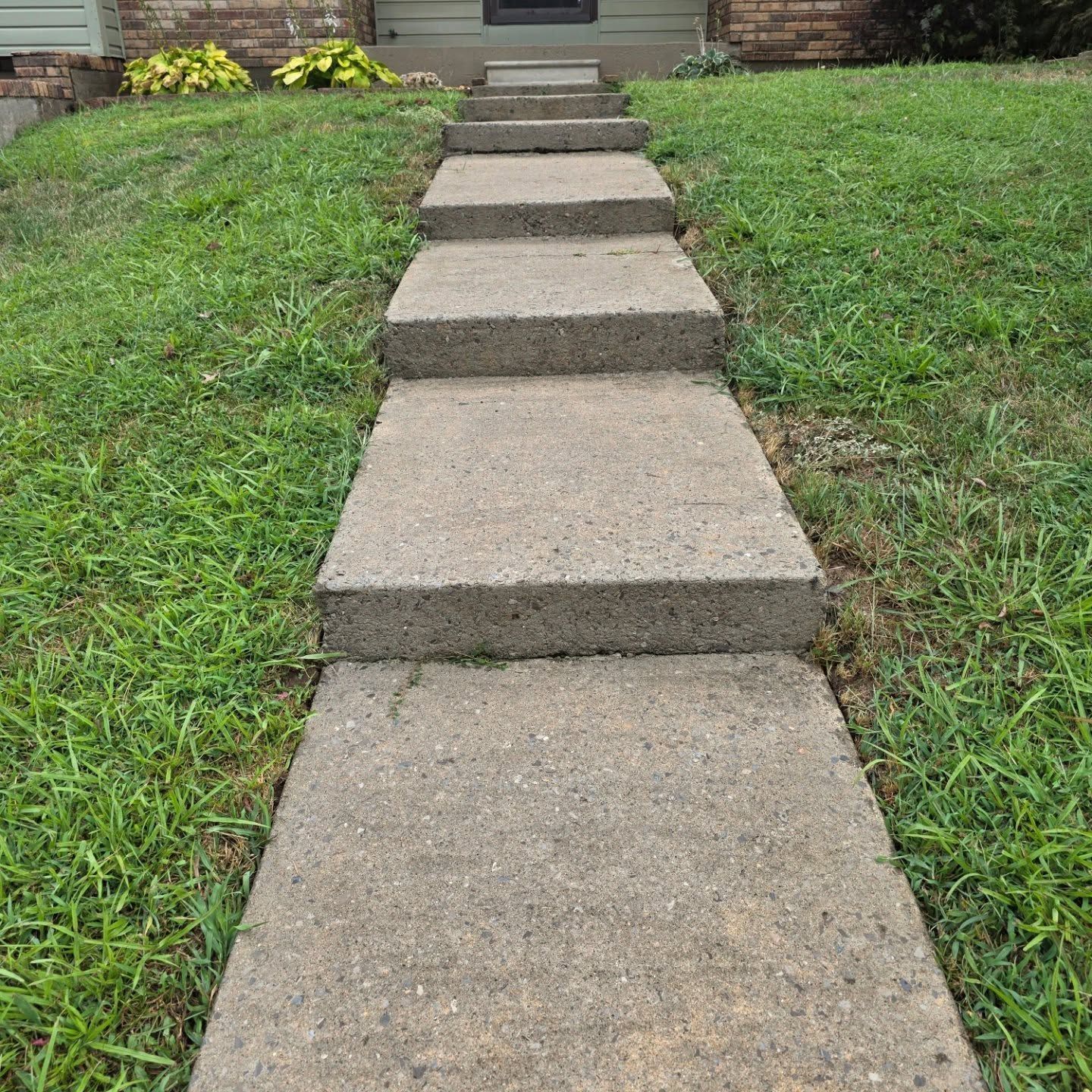 Concrete stepping stones leading to a house entrance through green grass