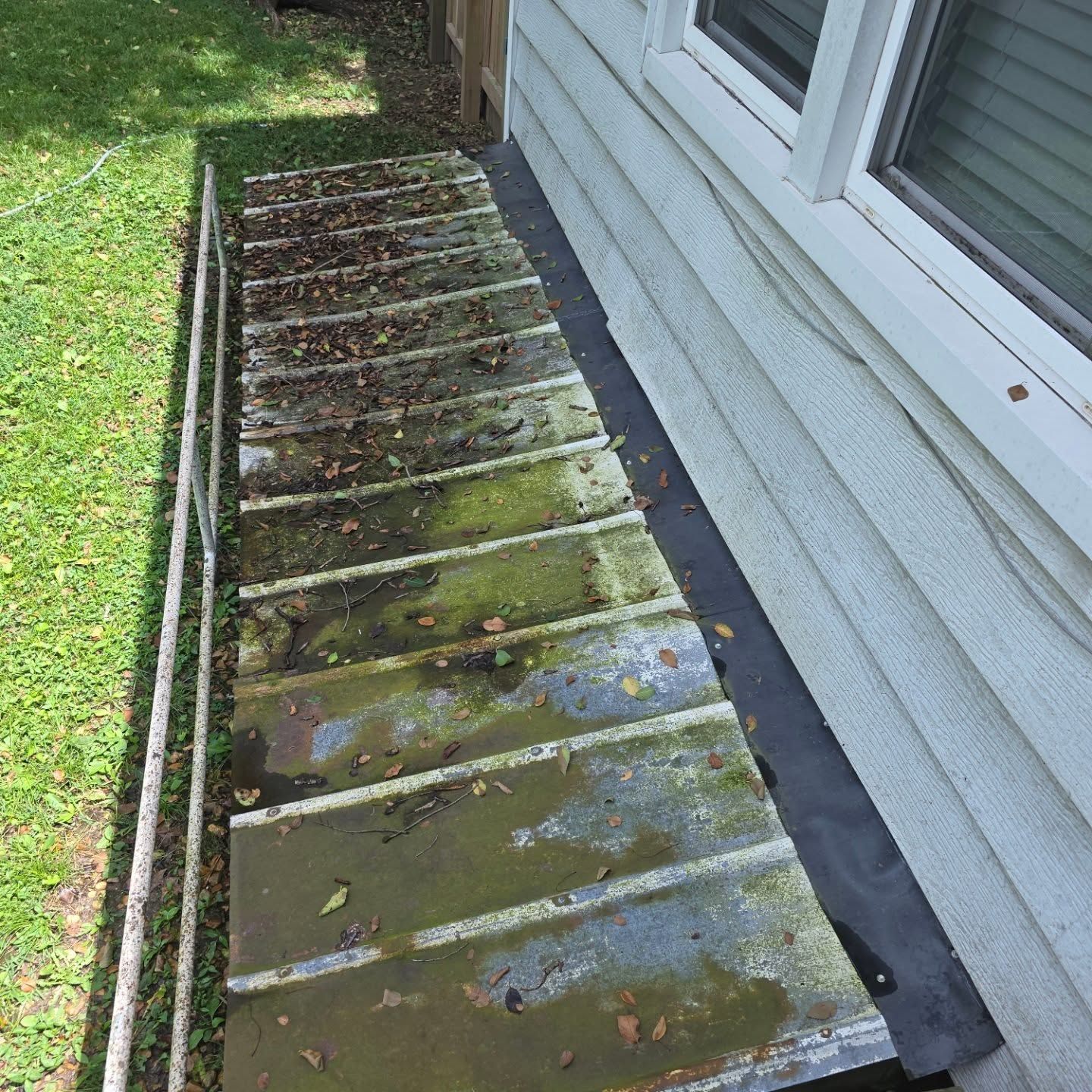 Moss-covered wooden ramp beside a house, with grass along one side.