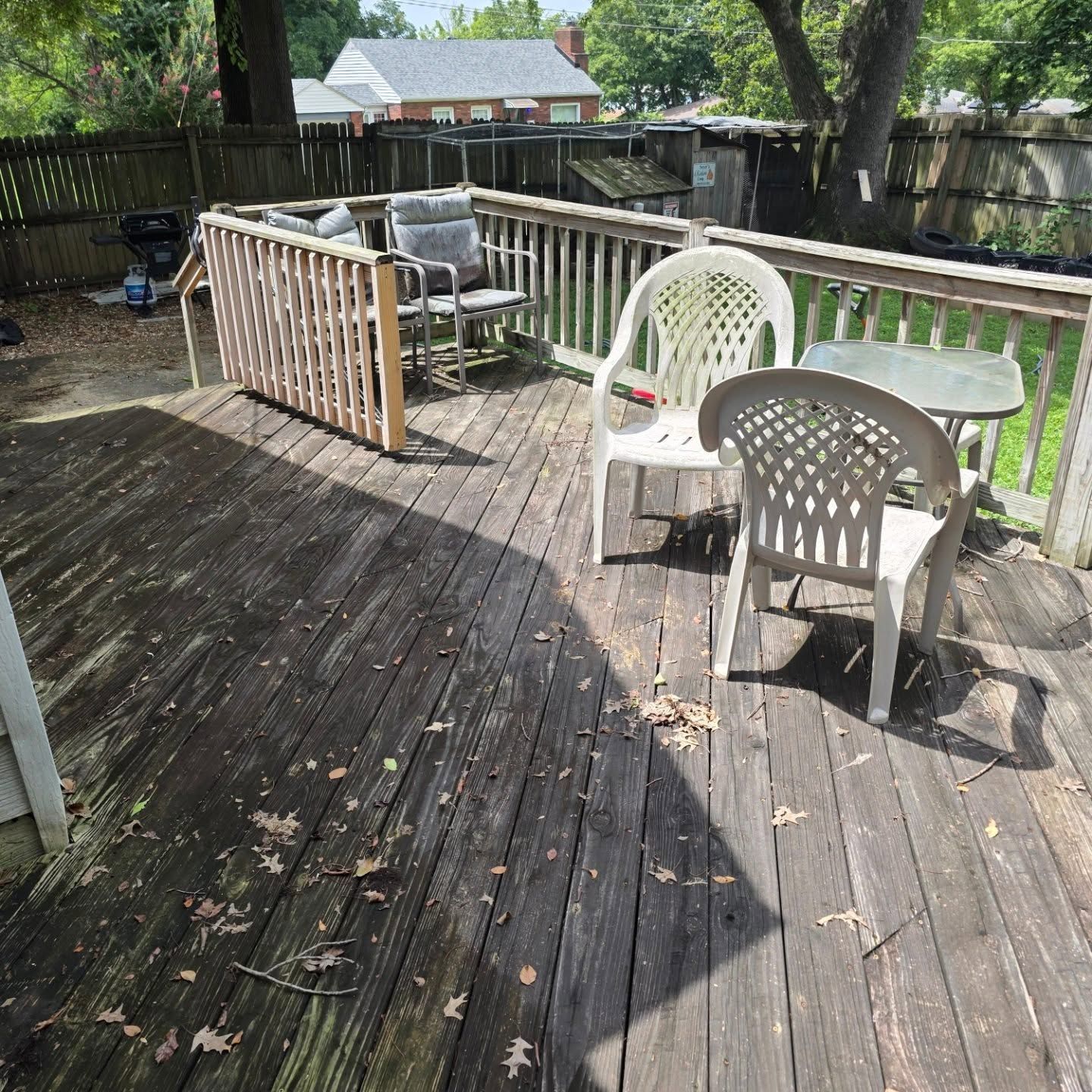 Wooden deck with white plastic chairs and table in a sunny backyard.
