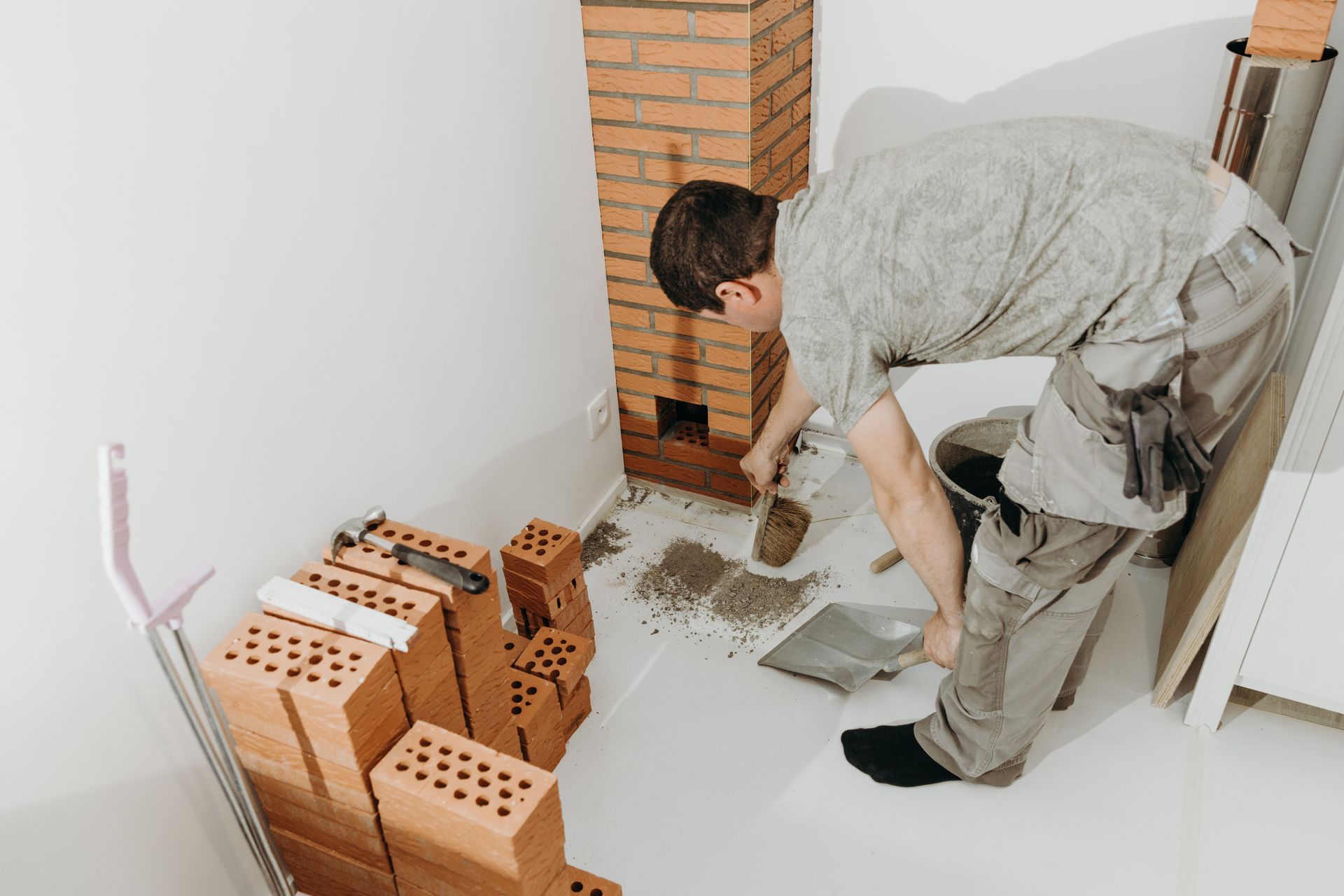 A person building a brick structure, kneeling, with tools and materials on the floor.