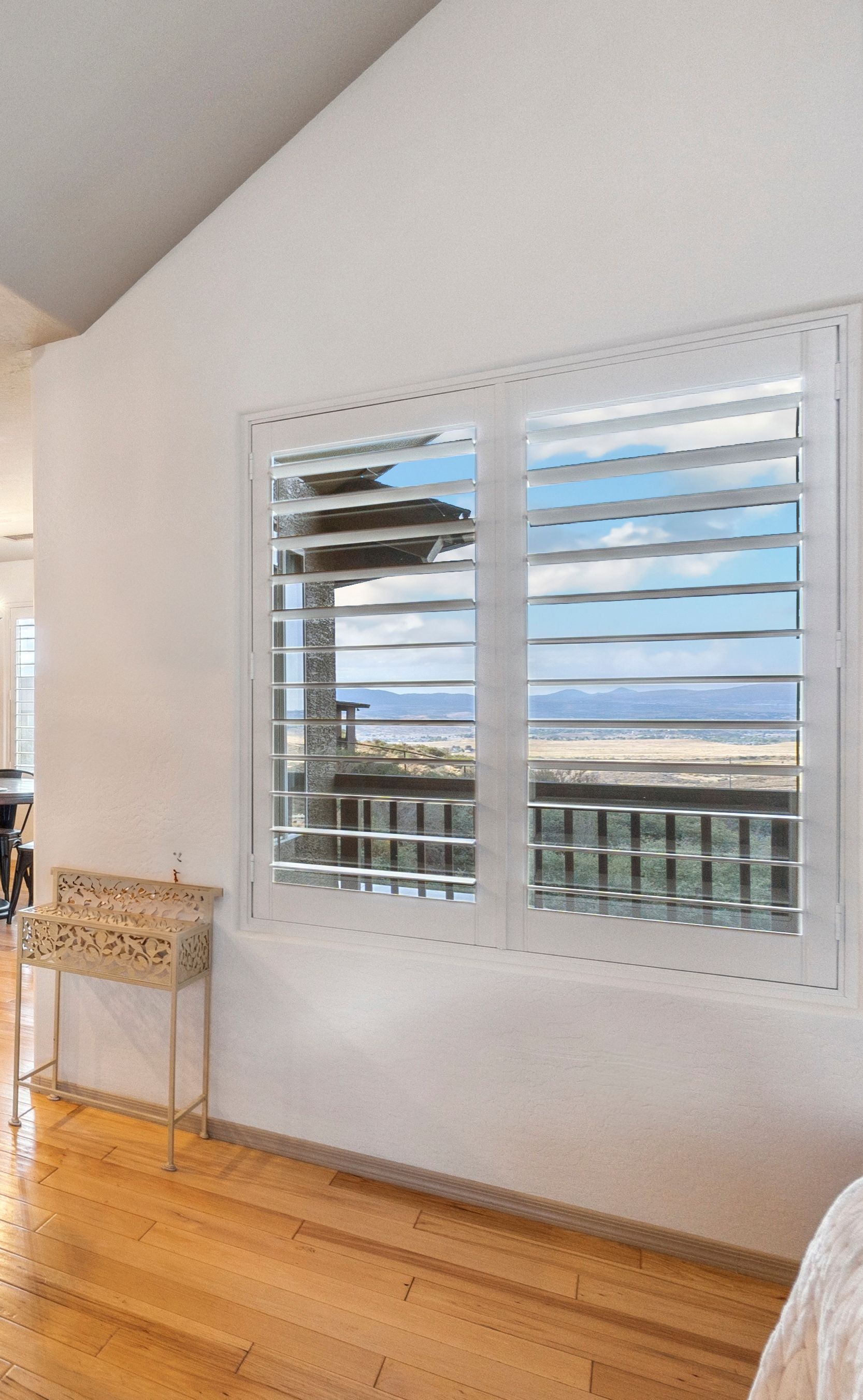 A room with wooden flooring, featuring a white wall and plantation shutters that overlook a scenic view outside A room with wooden flooring, featuring a white wall and plantation shutters that overlook a scenic view outside