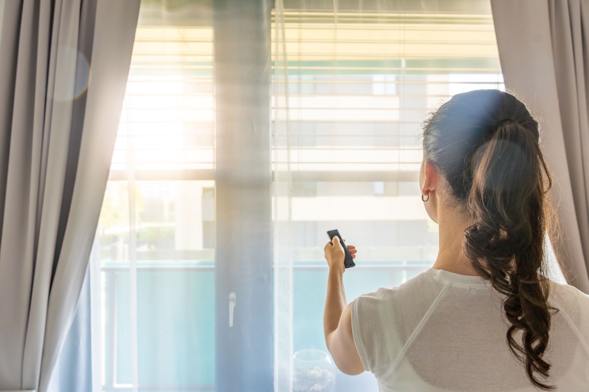 A woman is using a control to open her blinds.