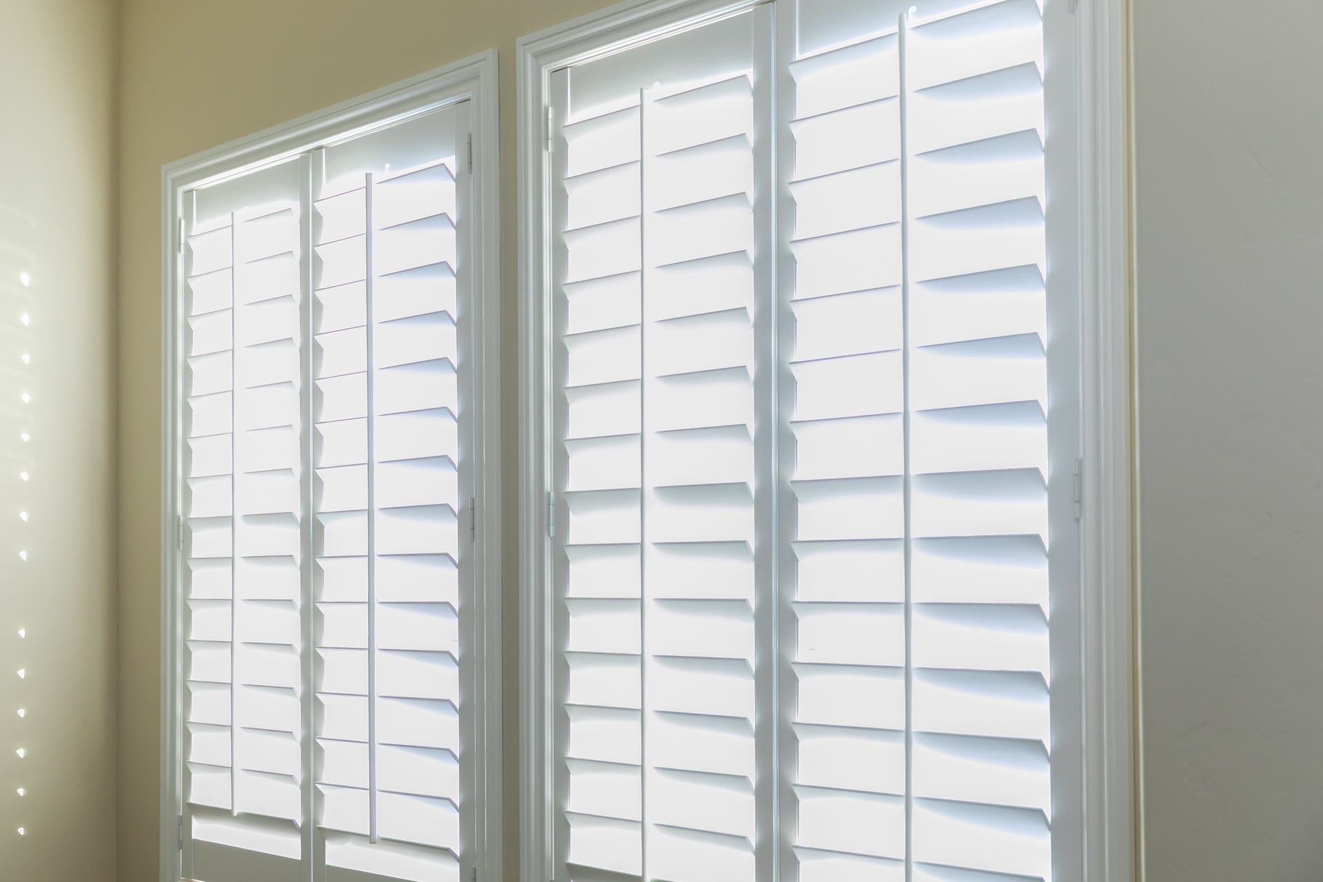 A set of open white plantation shutters in a light butter-yellow room. A set of open white plantation shutters in a light butter-yellow room.
