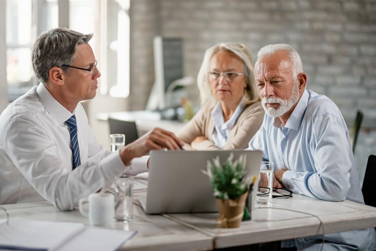 Three people discuss a laptop at a table in a bright office.
