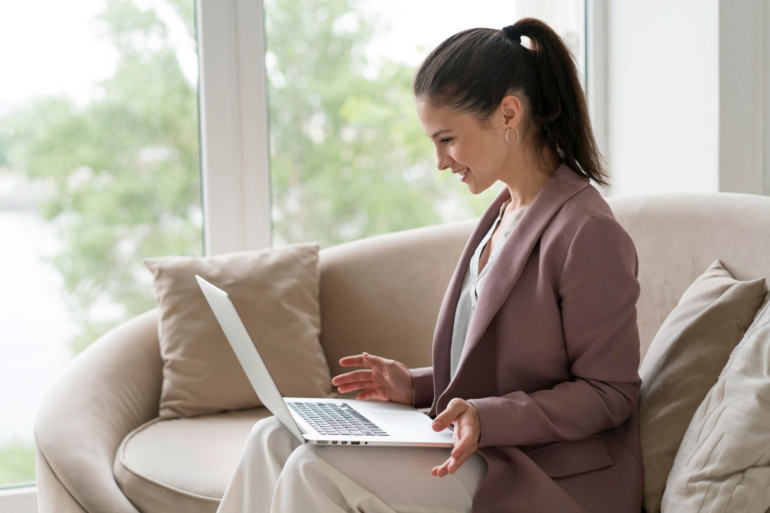 Woman using a laptop on a beige sofa in a bright living room