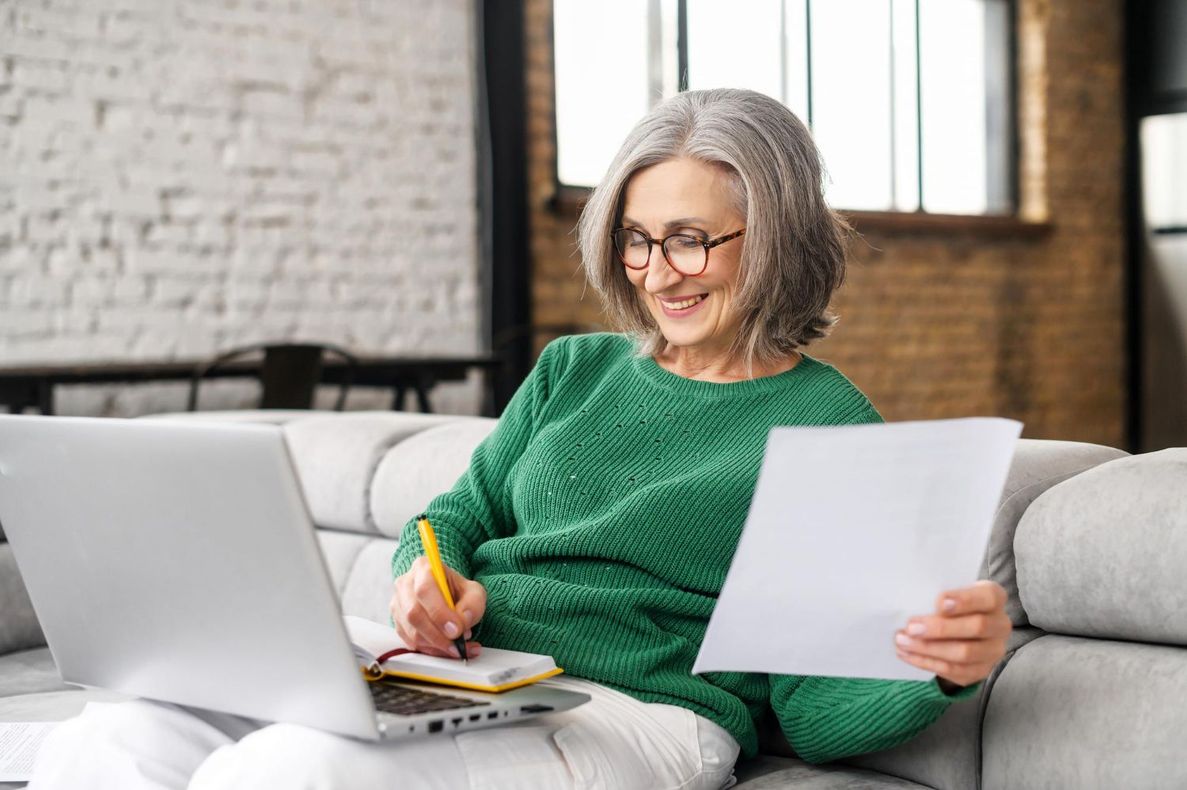 Woman in green sweater working on a laptop and reviewing papers on a couch