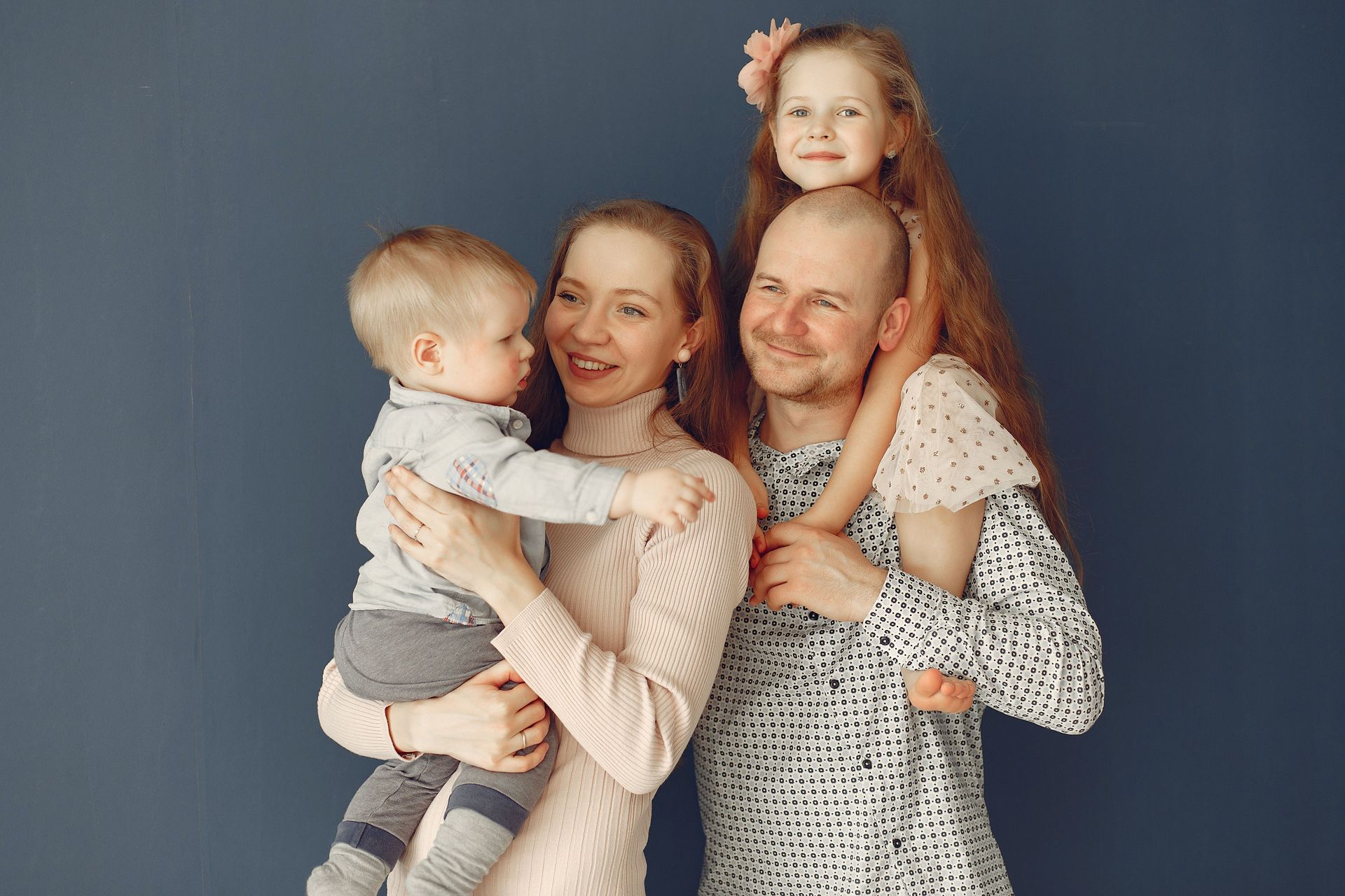 Family of four posing against a blue backdrop, smiling and holding two children.