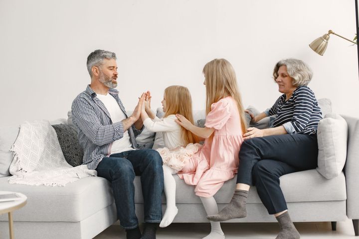 Family playing a hand-clapping game on a white couch in a bright living room