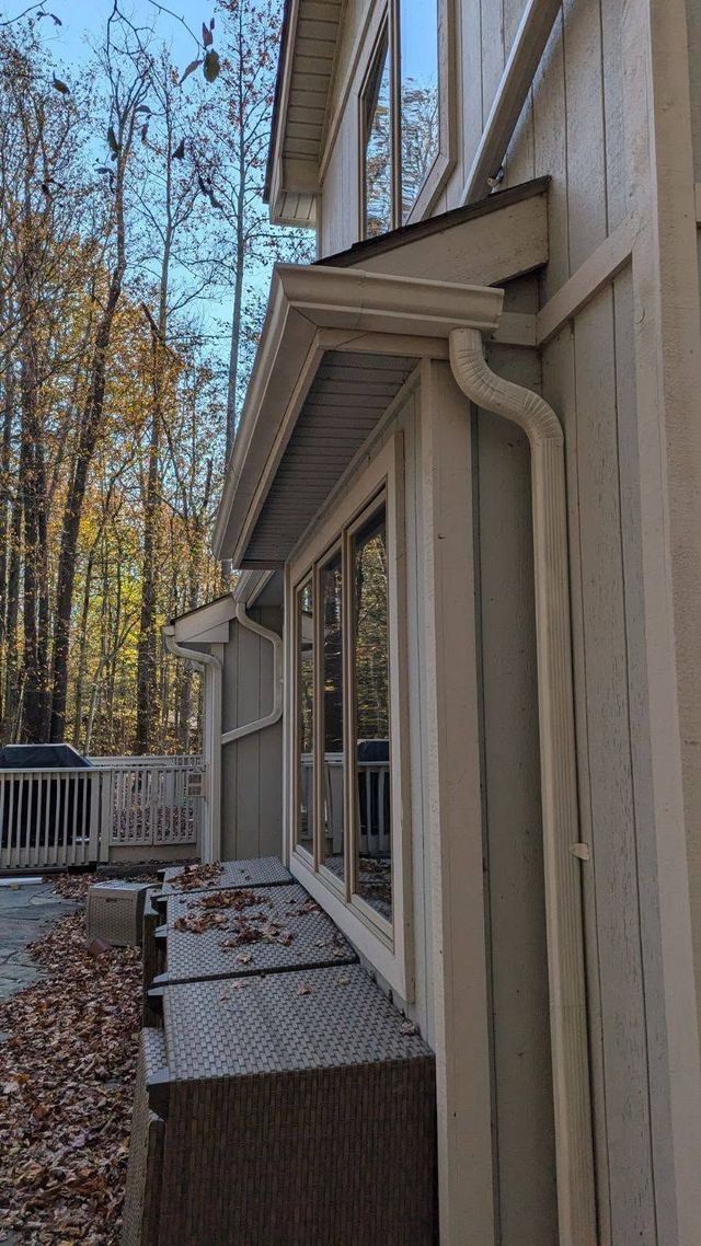 Side view of a house with beige siding, windows, and a small deck beside autumn trees