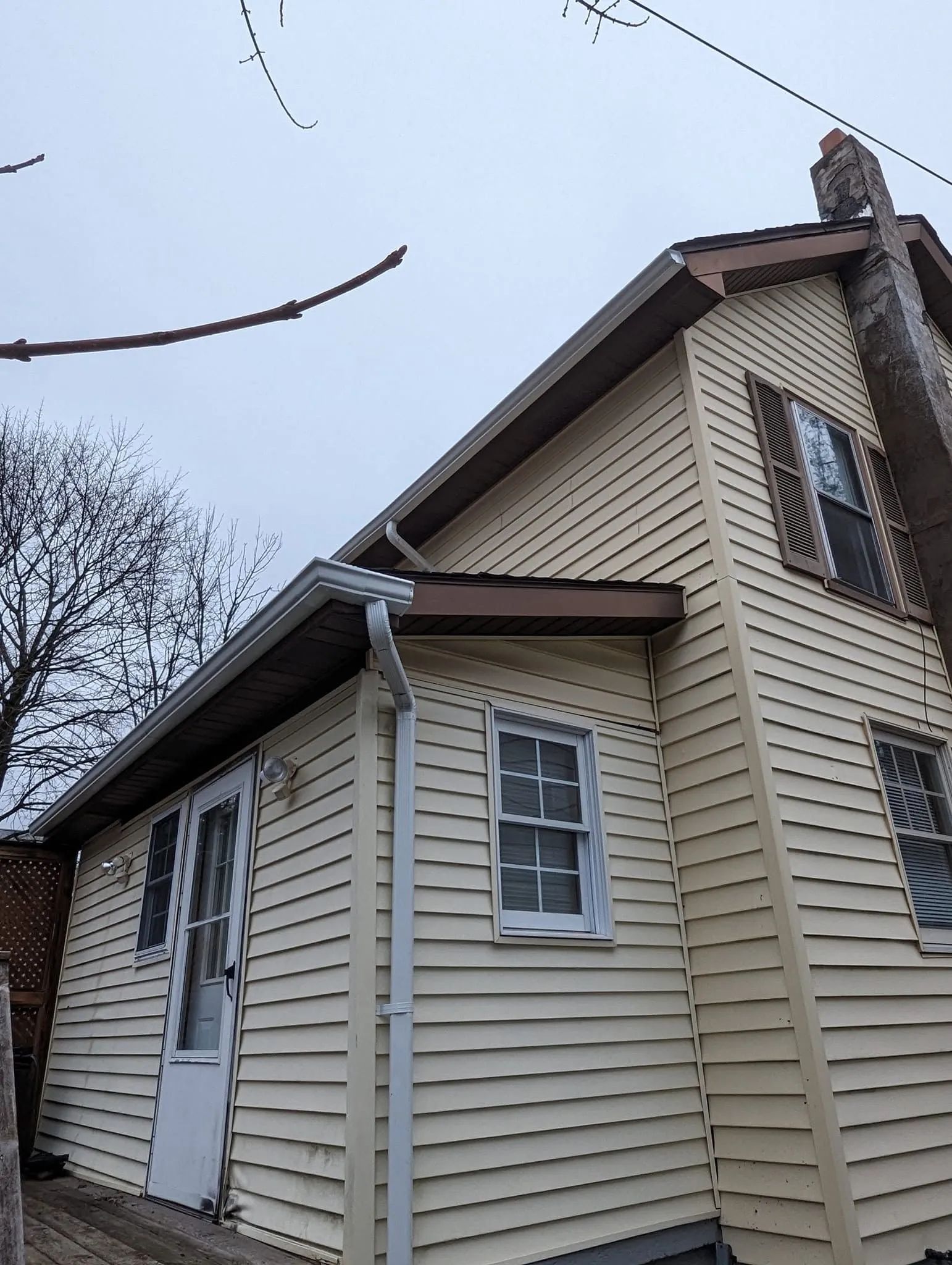Small beige house with white trim and a front door, viewed from the side under a cloudy sky