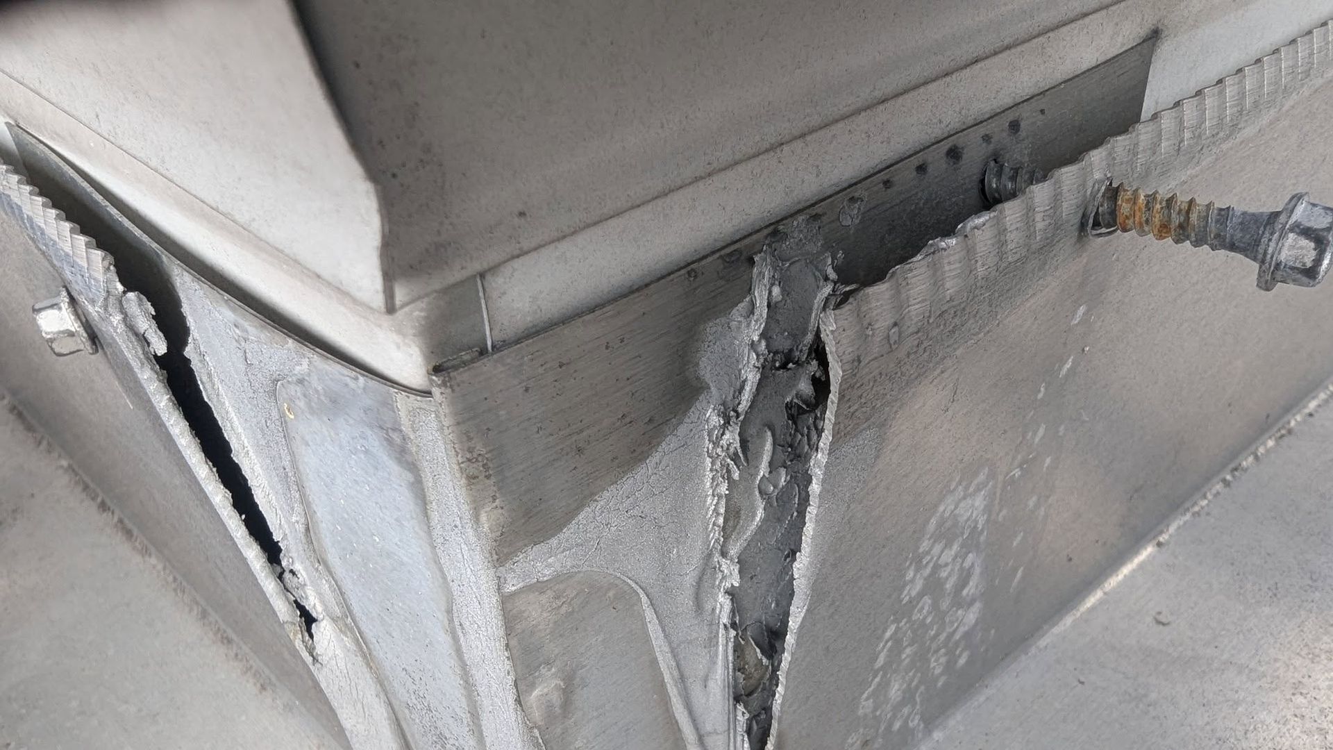 Close-up of torn gray upholstery with exposed stitching and a damaged seam on a metal frame