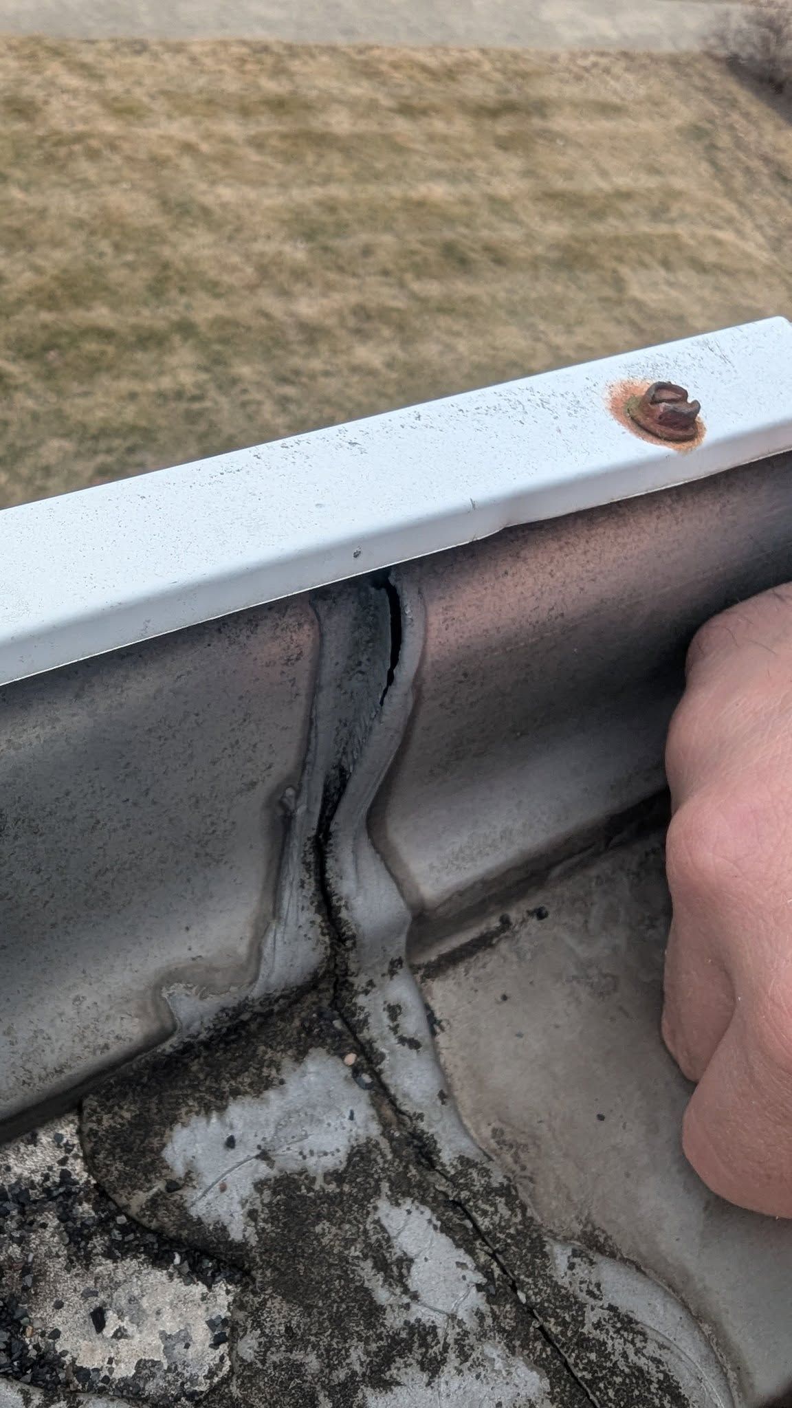 Close-up of a weathered window sill with peeling sealant and a hand holding the frame.