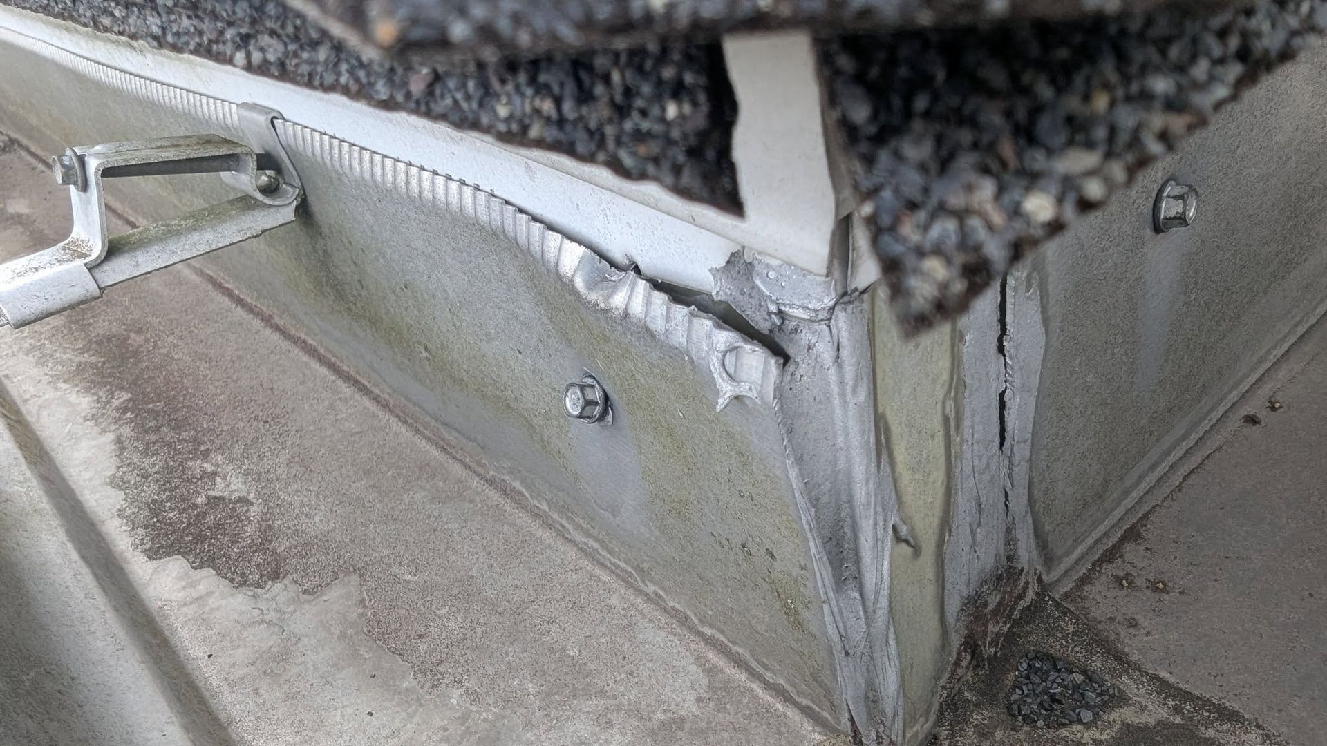 Close-up of a dirty metal corner seam with peeling white caulk and worn gray flooring.