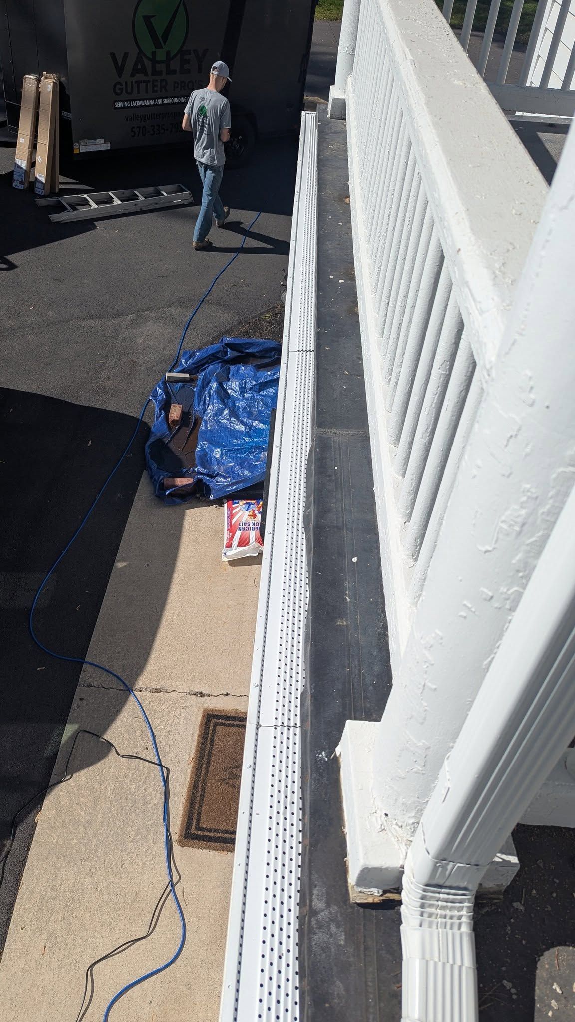 Person kneels beside blue tarp on sidewalk next to white fence and coiled blue rope