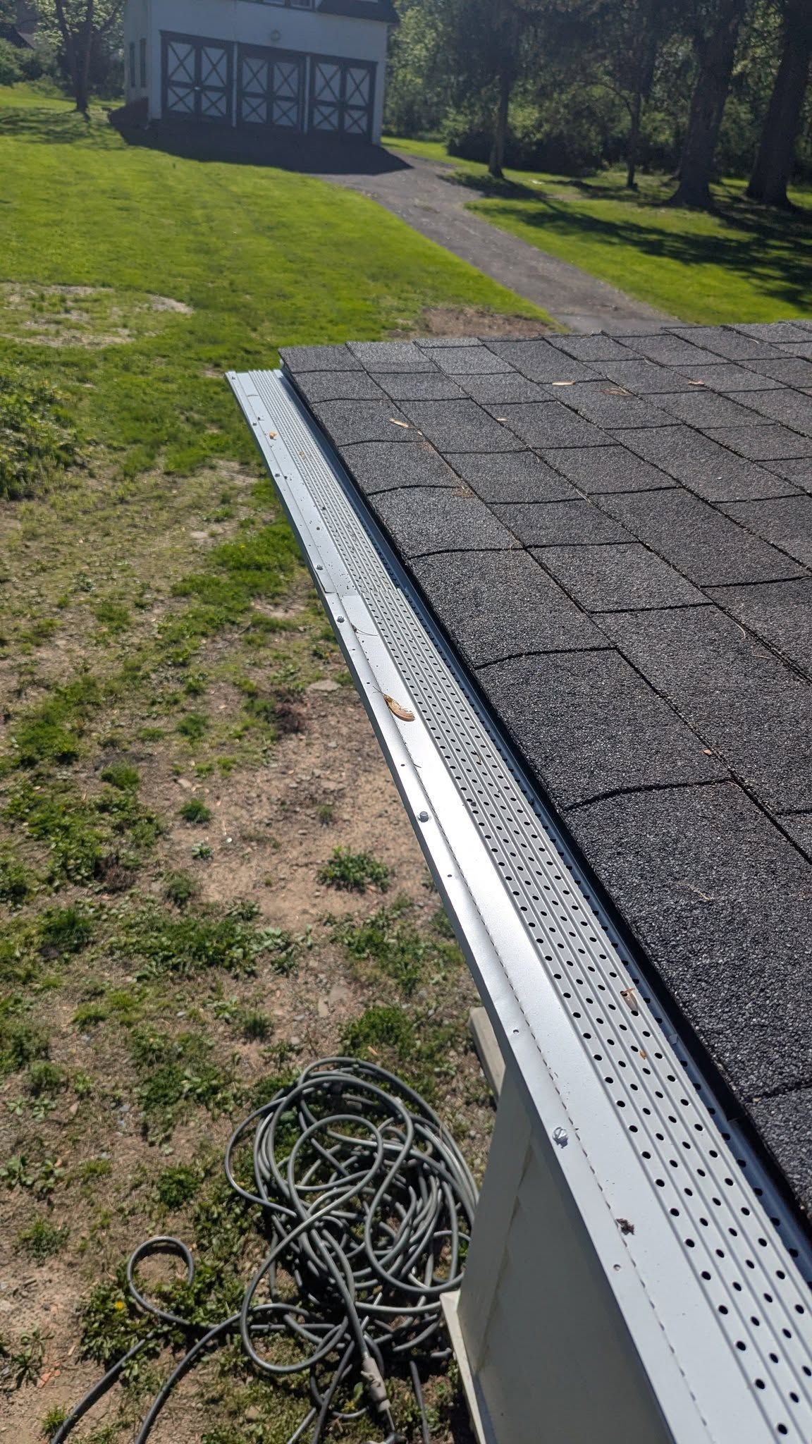 Roof edge with gray shingles and white drip edge, beside a grassy yard and a coiled cable on the ground