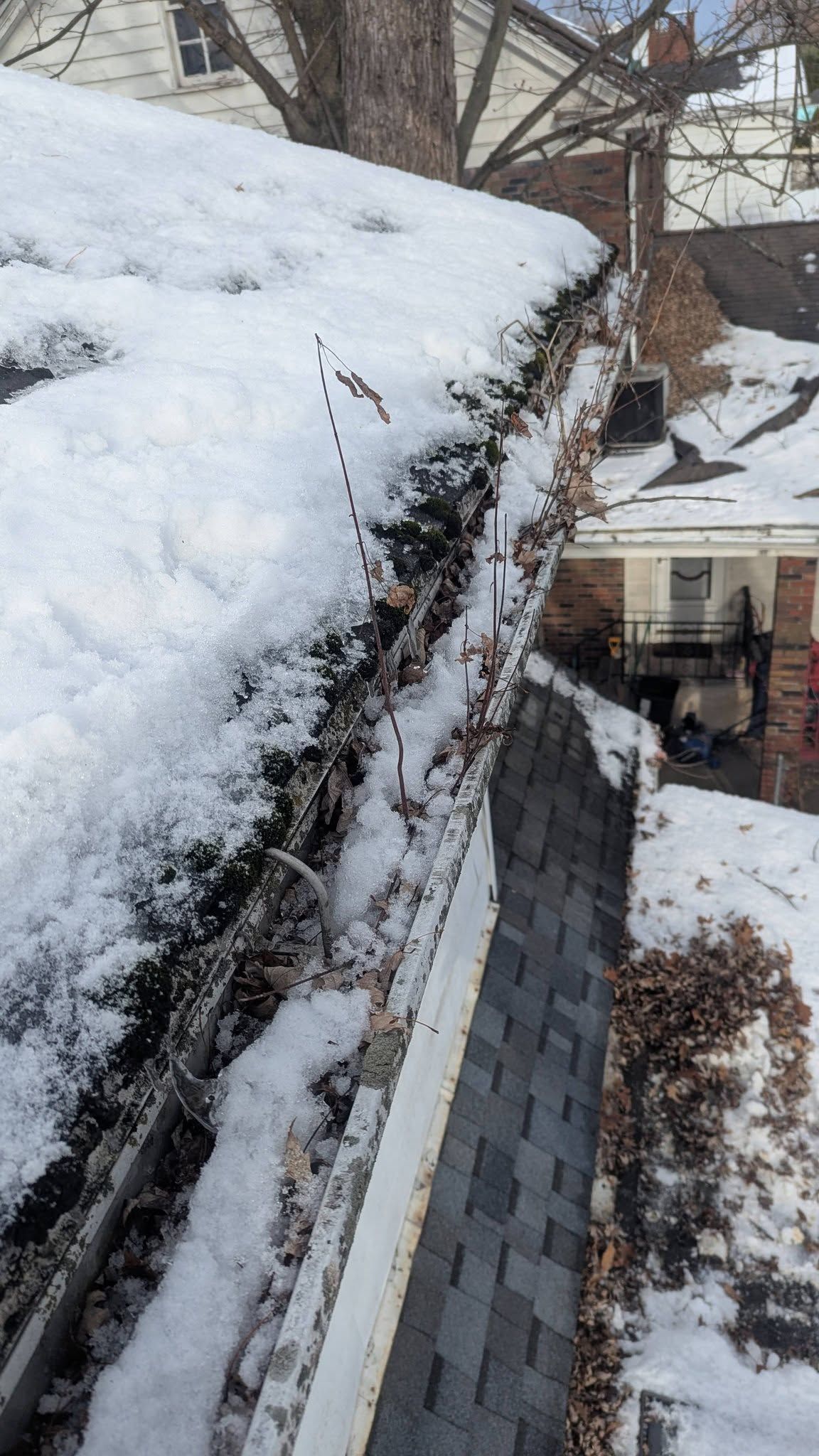 Snow-covered roof edge with icicles above a dark shingled side wall and a snowy yard below.