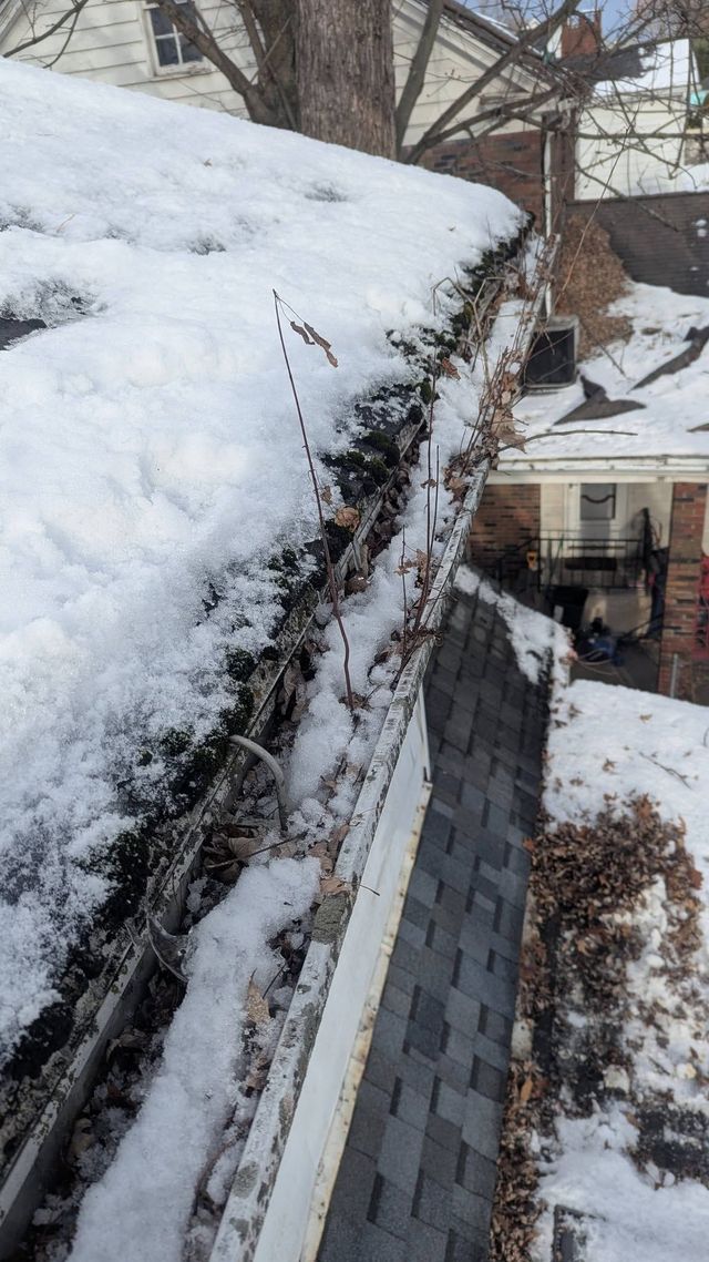 Snow-covered roof edge above a dark shingled wall beside a snowy residential yard