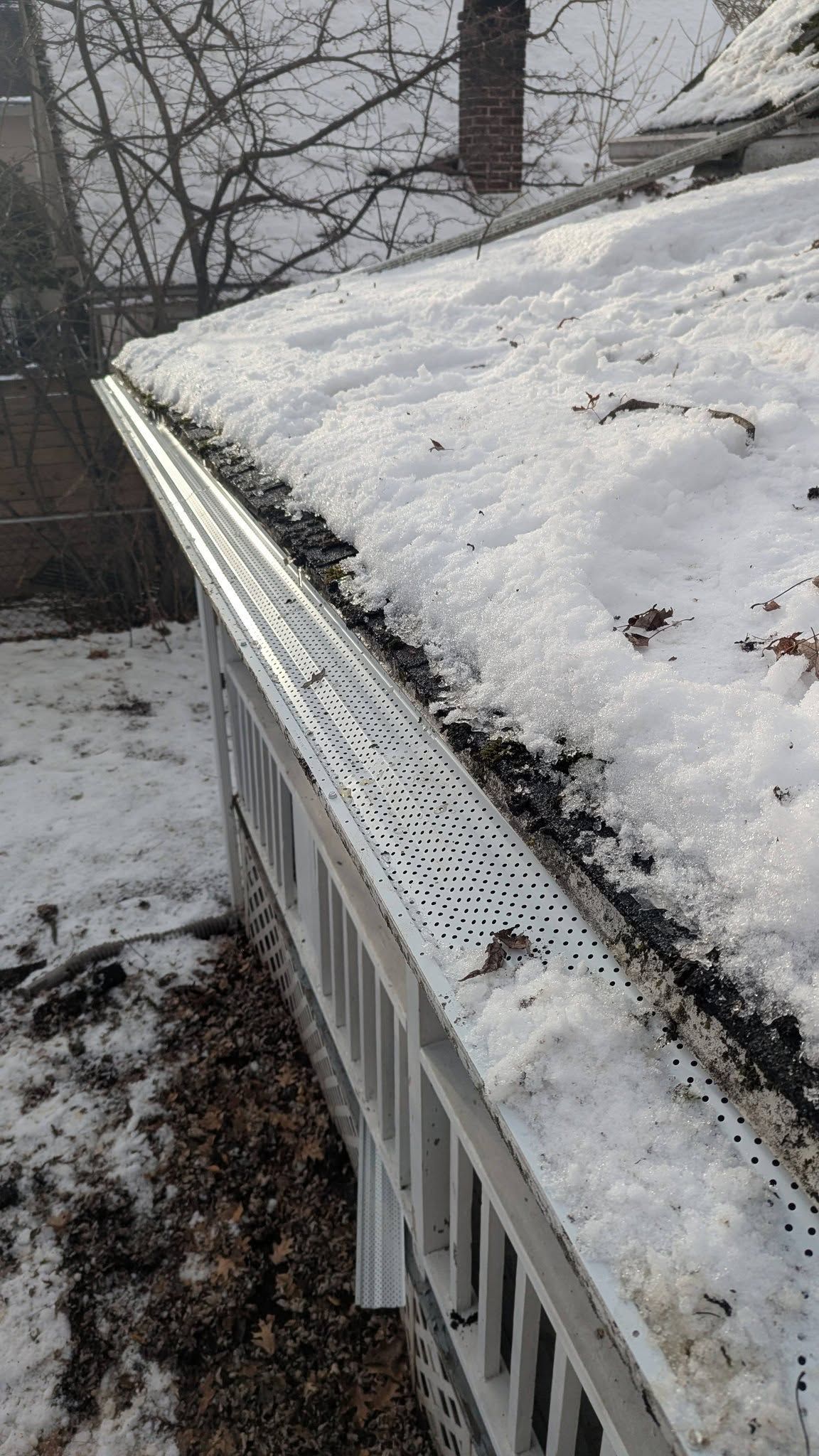 Snow-covered roof edge with gutters, viewed from above in a wintry outdoor setting