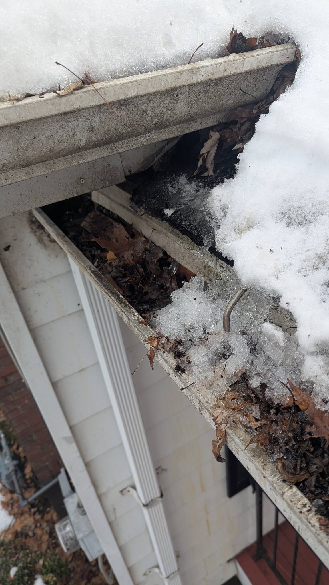 Snow-covered roof with debris and exposed soffit damage near the gutter