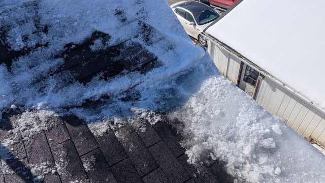 Snow-covered rooftop beside a white building, with a car partially visible below.