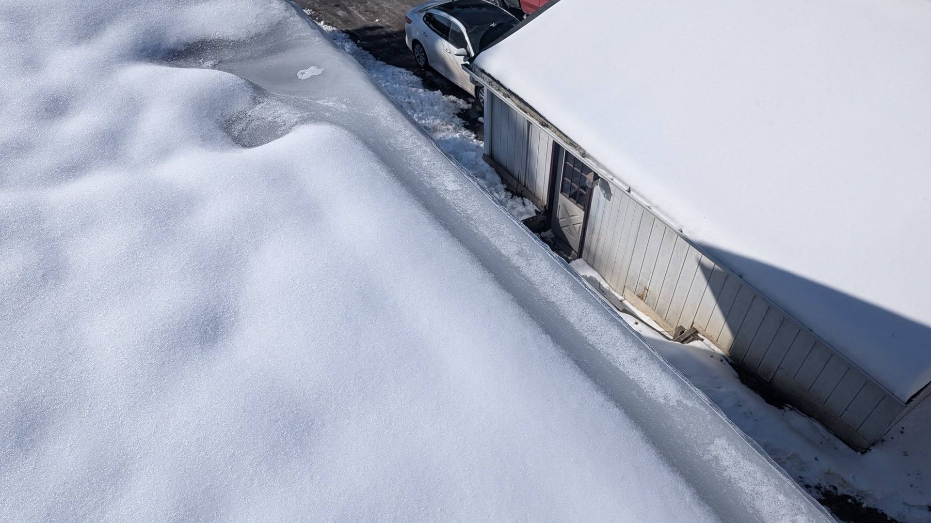 Snow-covered rooftop edge with a metal gutter and a white wall.