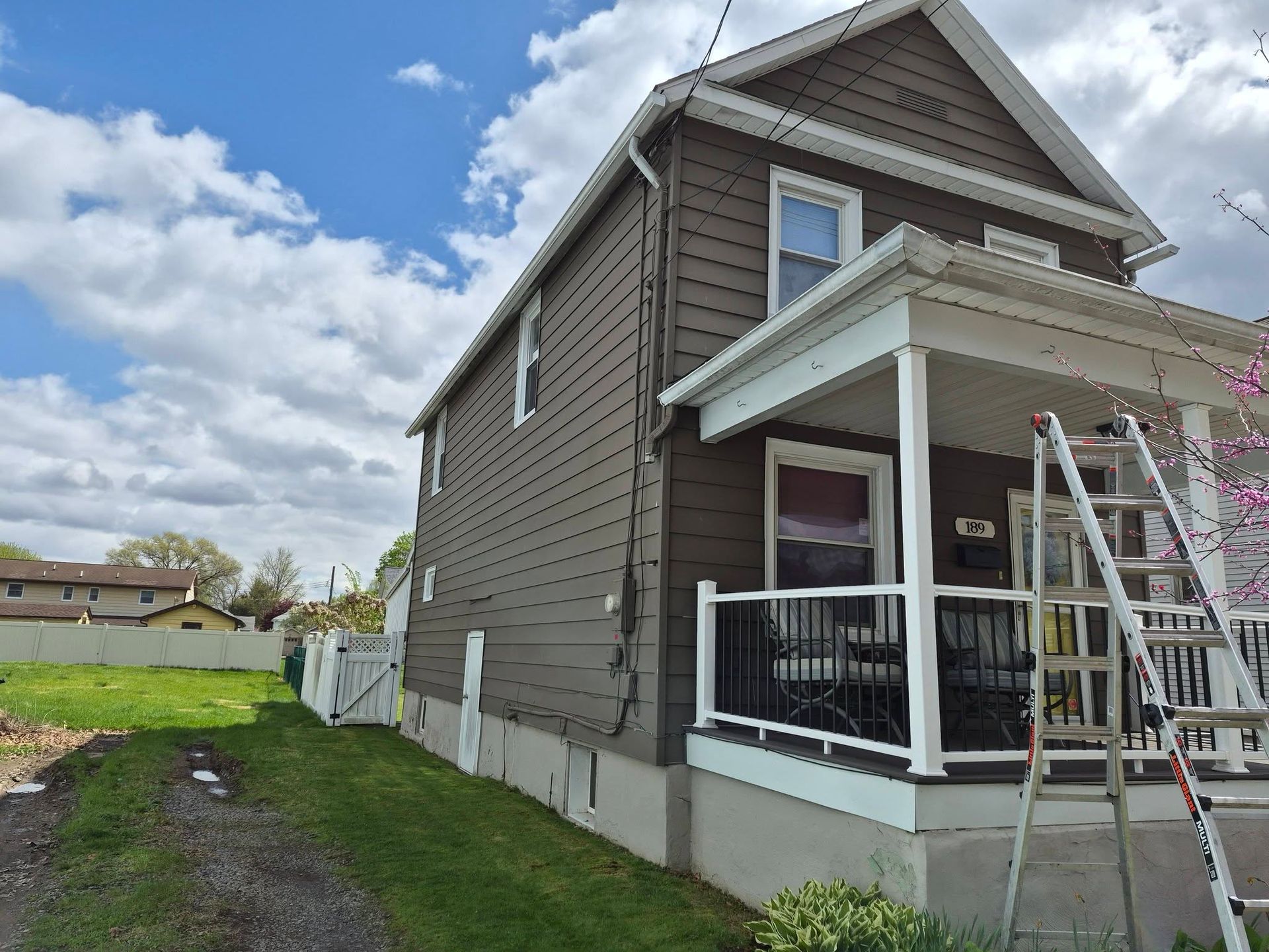 Two-story house exterior with porch, ladder, and partly visible siding repair work