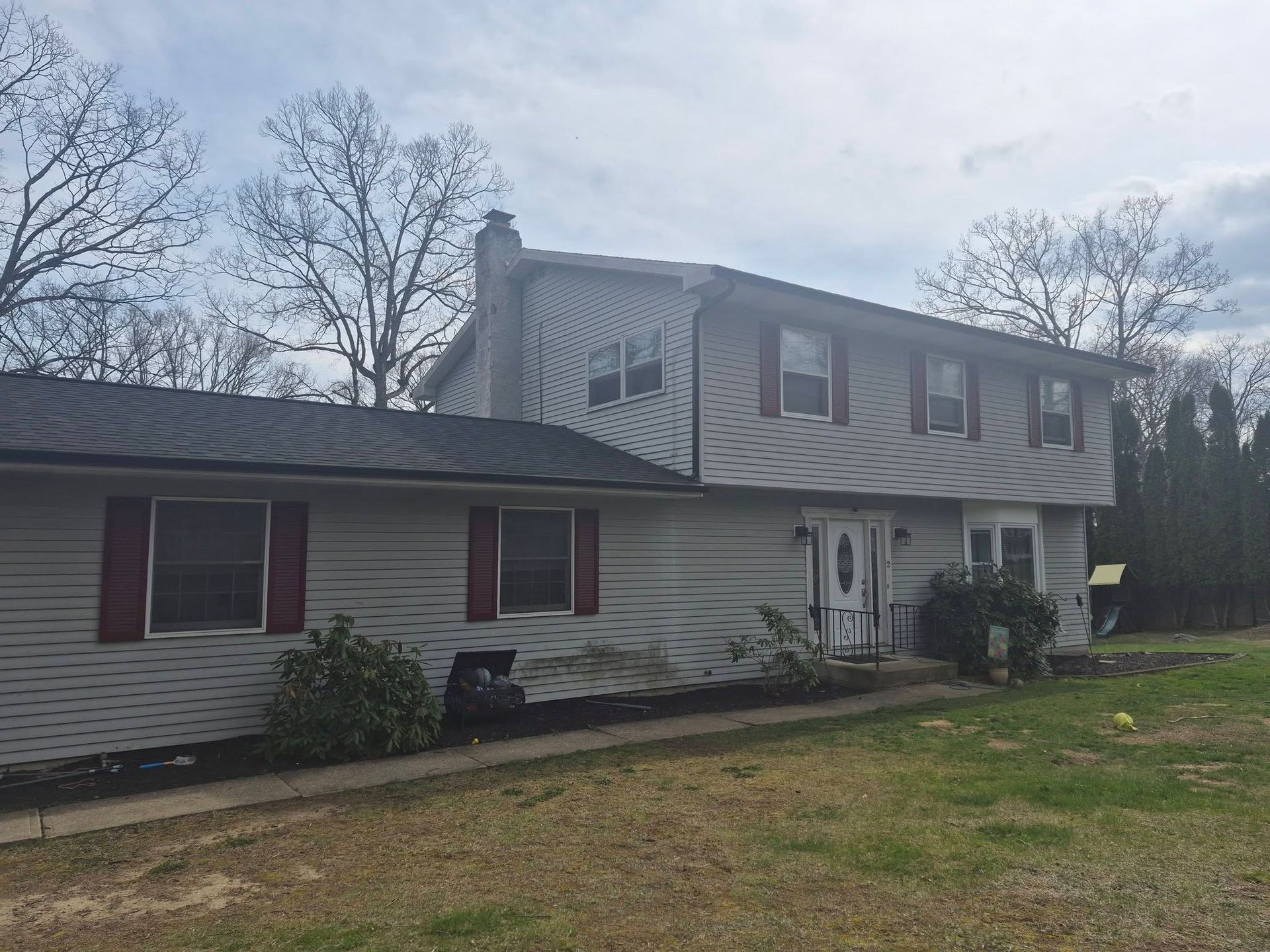 Suburban house with gray siding, red shutters, and a sloped roof under a cloudy sky