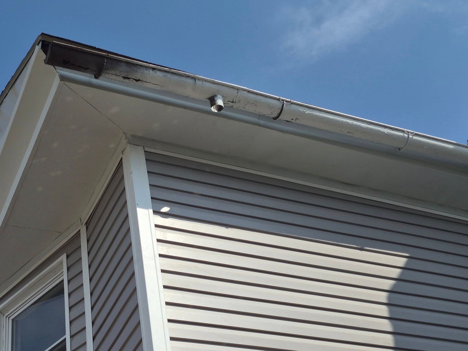 House exterior with gray siding, white trim, and a roof edge against a blue sky
