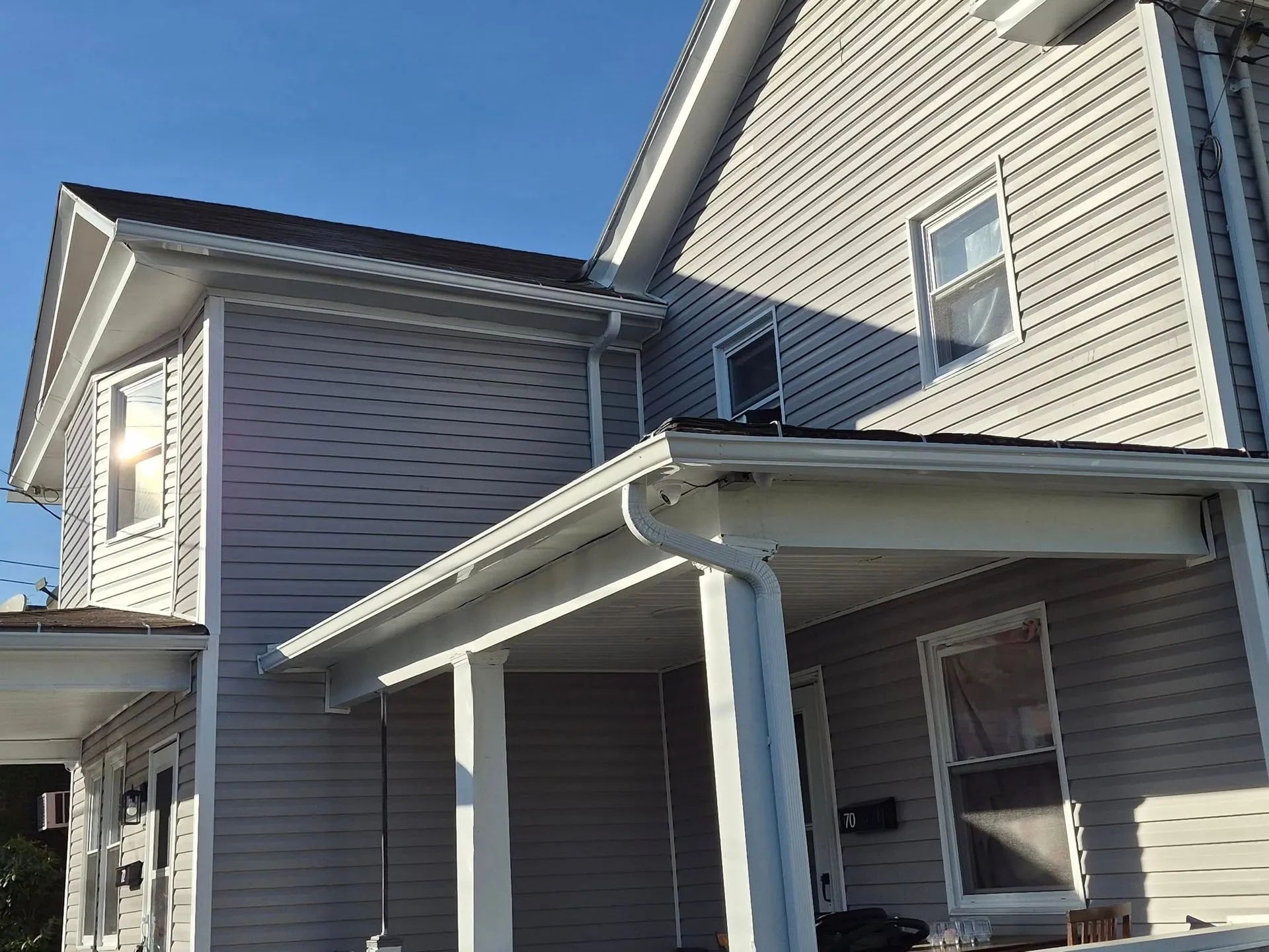 Gray house exterior with white trim and covered porch under a clear blue sky
