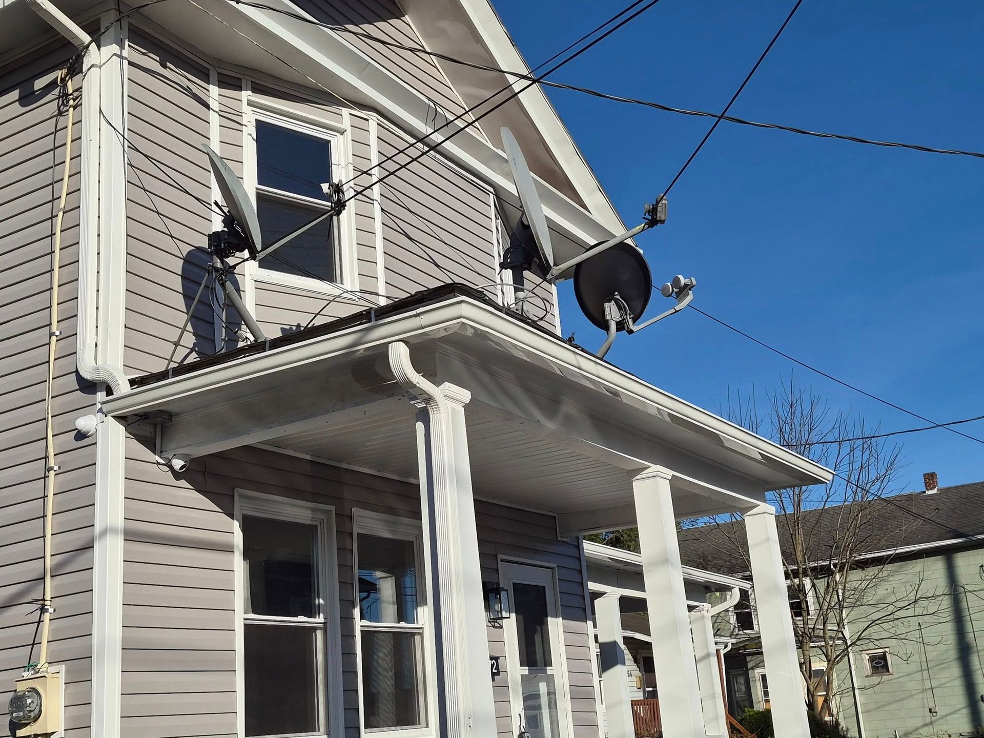 Two-story gray house with white trim, front porch, satellite dish, and a second-floor window under repair