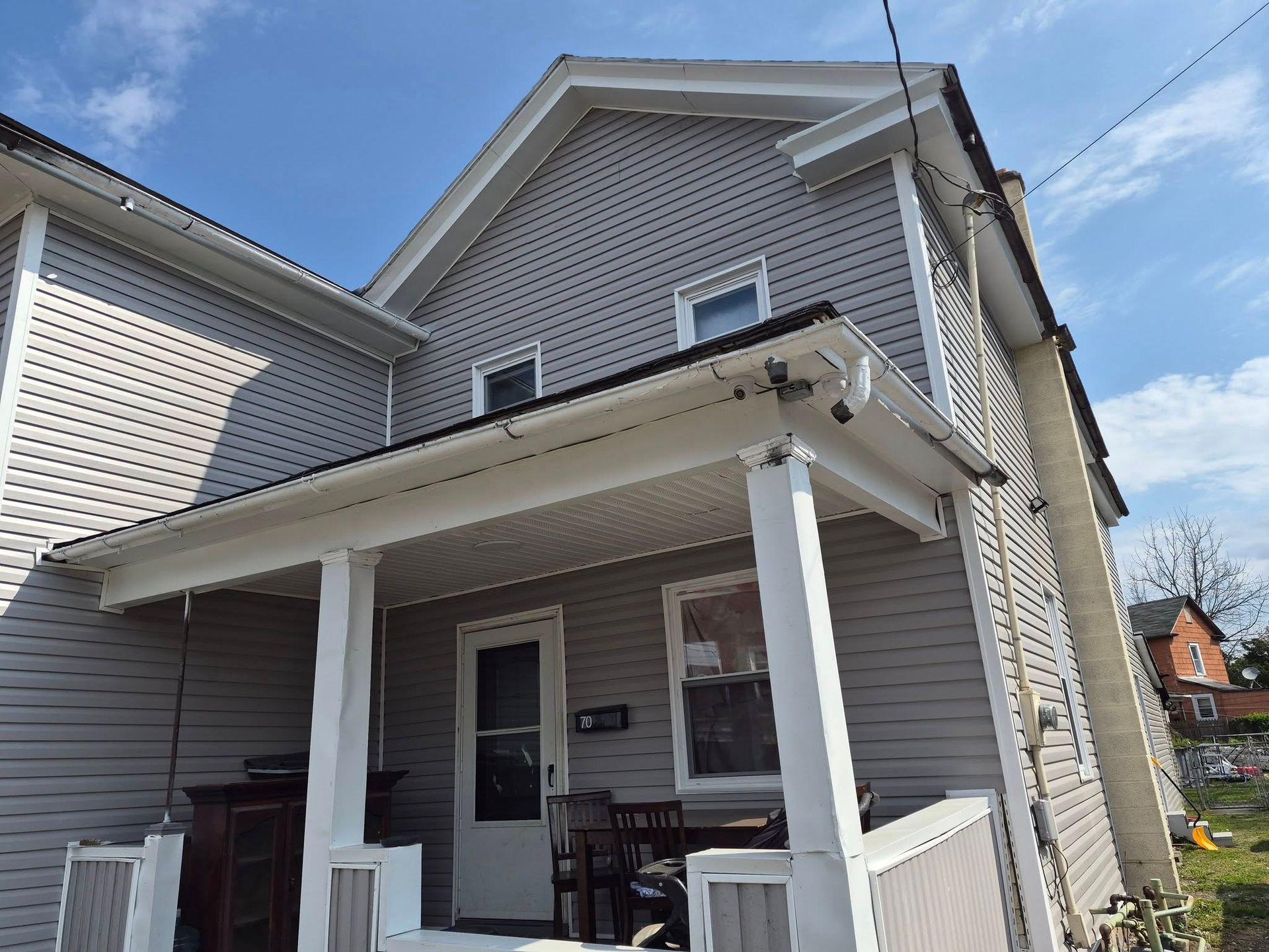 White two-story house with a small covered porch, white columns, and vinyl siding under a blue sky