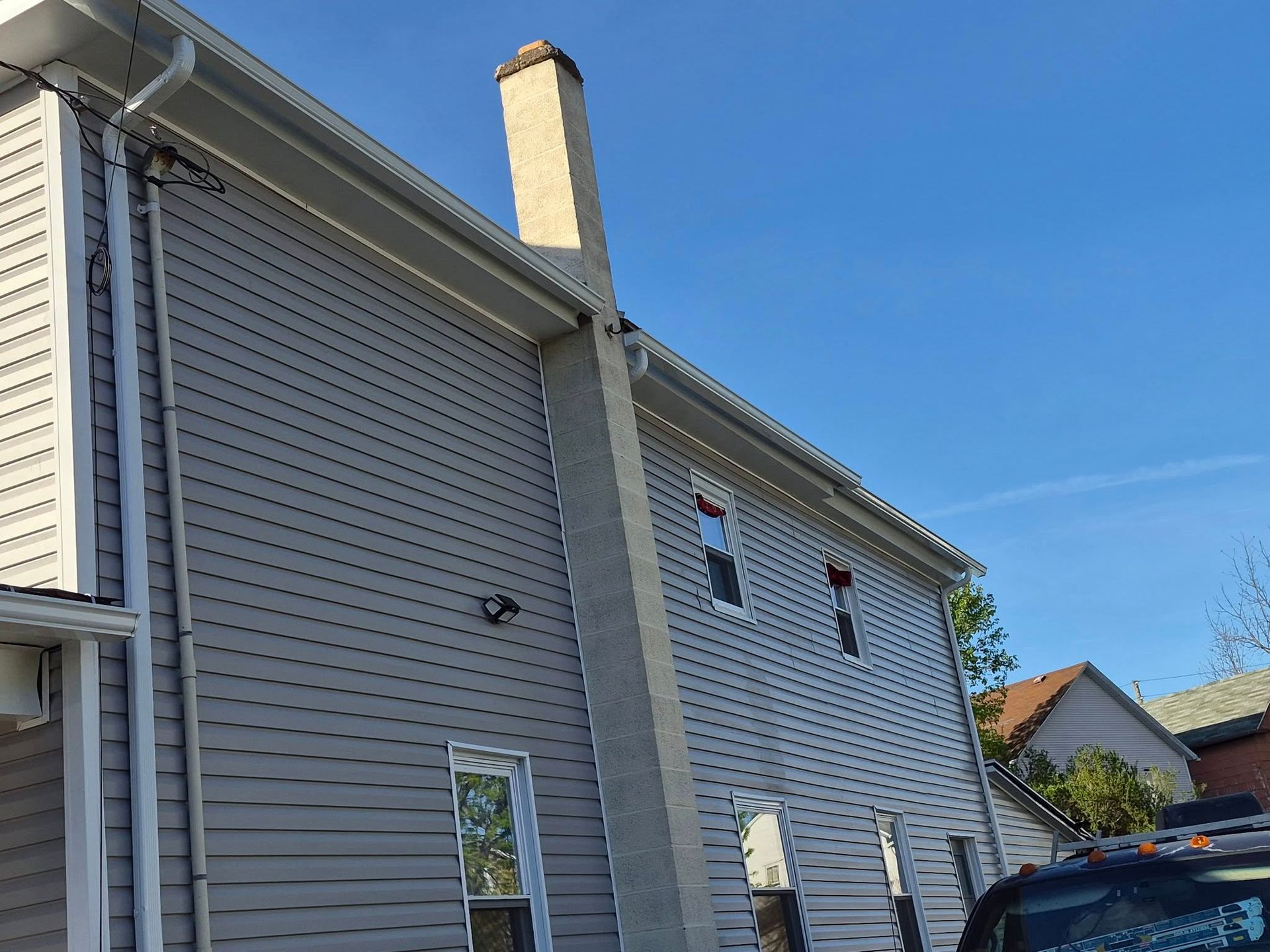 Gray house exterior with white trim, chimney, and blue sky overhead