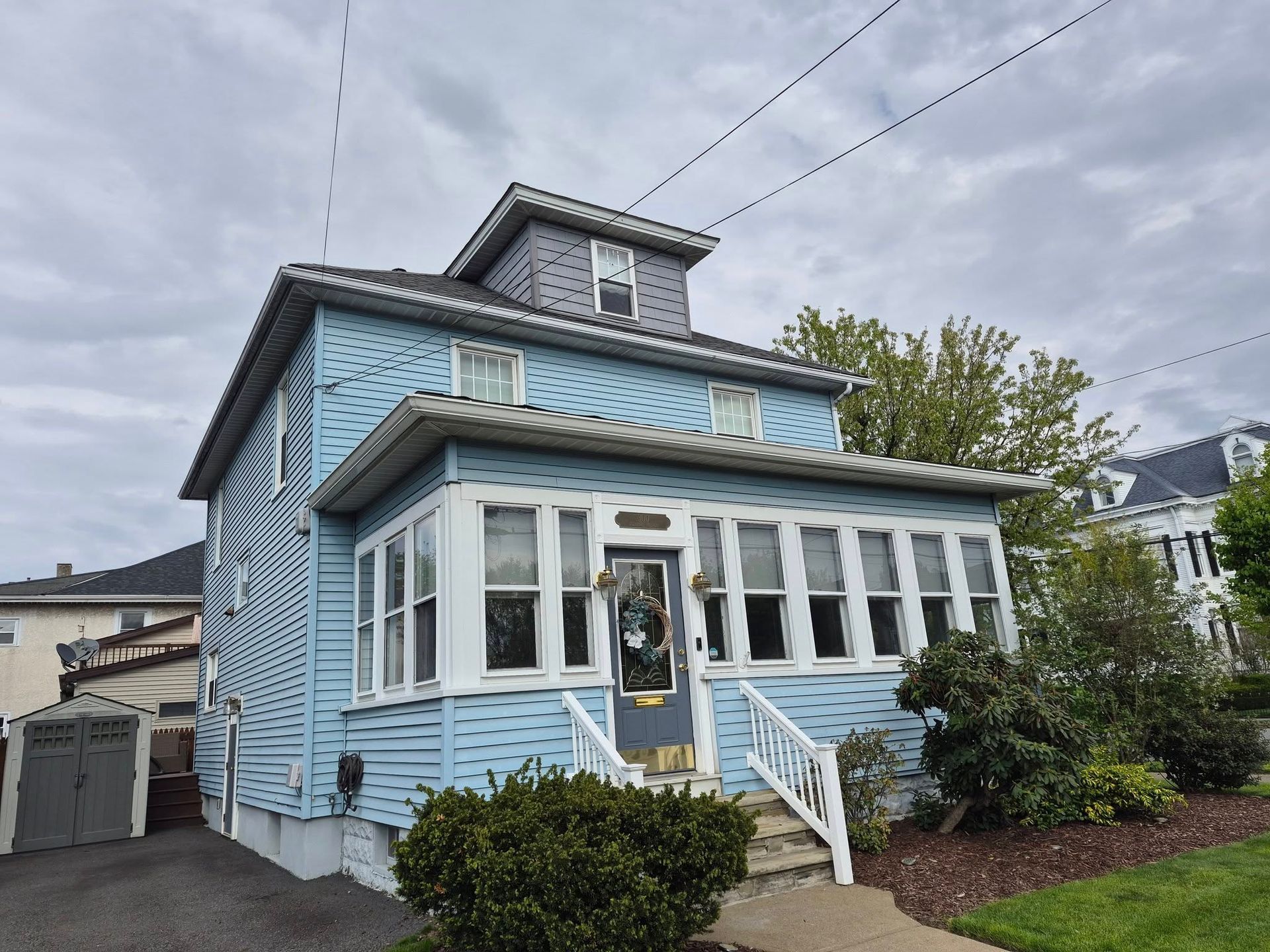 Light blue Victorian-style house with white trim and a front porch on a cloudy street