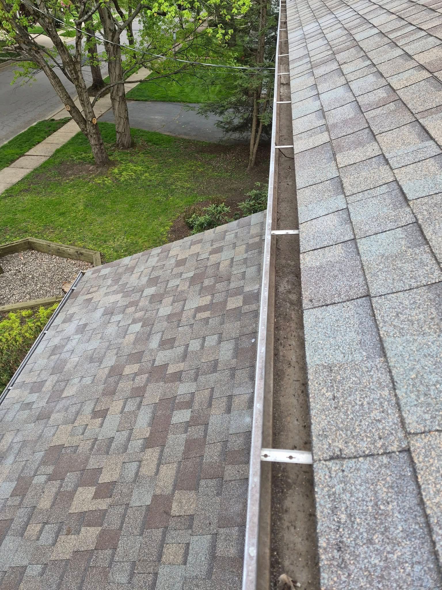 Roof and gutter view beside a sloped shingle roof, with trees and a lawn below