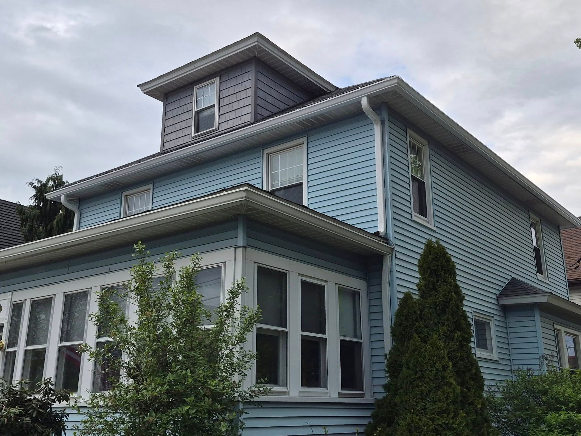 Light blue Victorian house with white trim and a wraparound porch under a cloudy sky