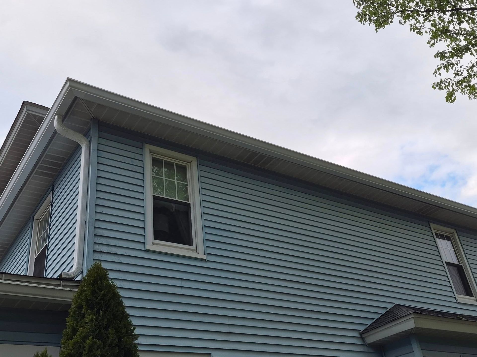 Blue house exterior with white trim and an open second-floor window under a cloudy sky