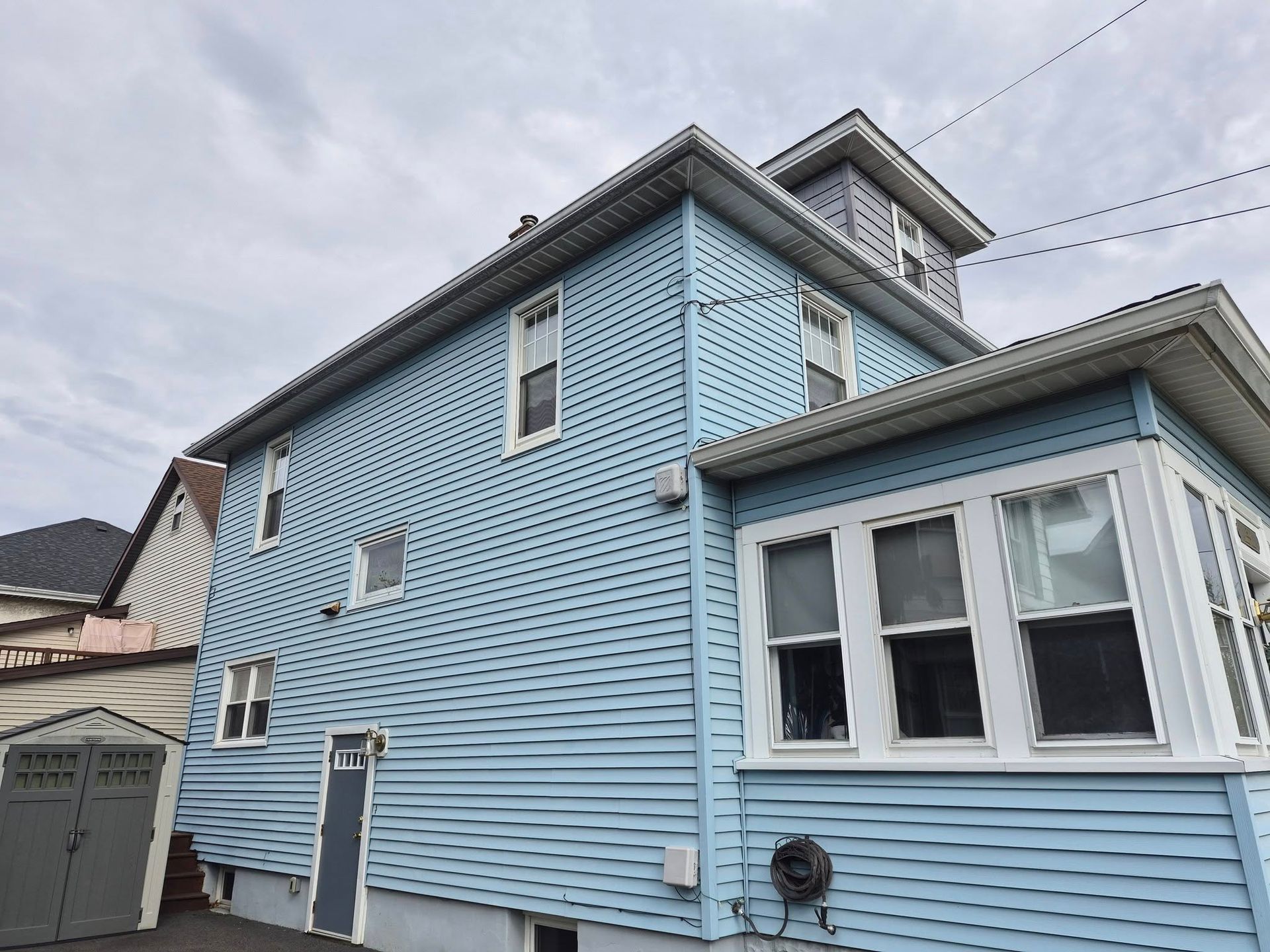 Light blue house exterior with white trim and a small bay window under a cloudy sky